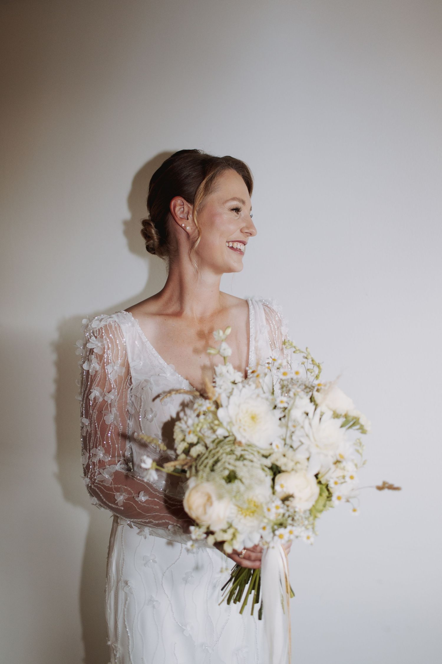 A series of elegant bridal portraits showing a white lace wedding dress and delicate white floral bouquet against a neutral wall.
