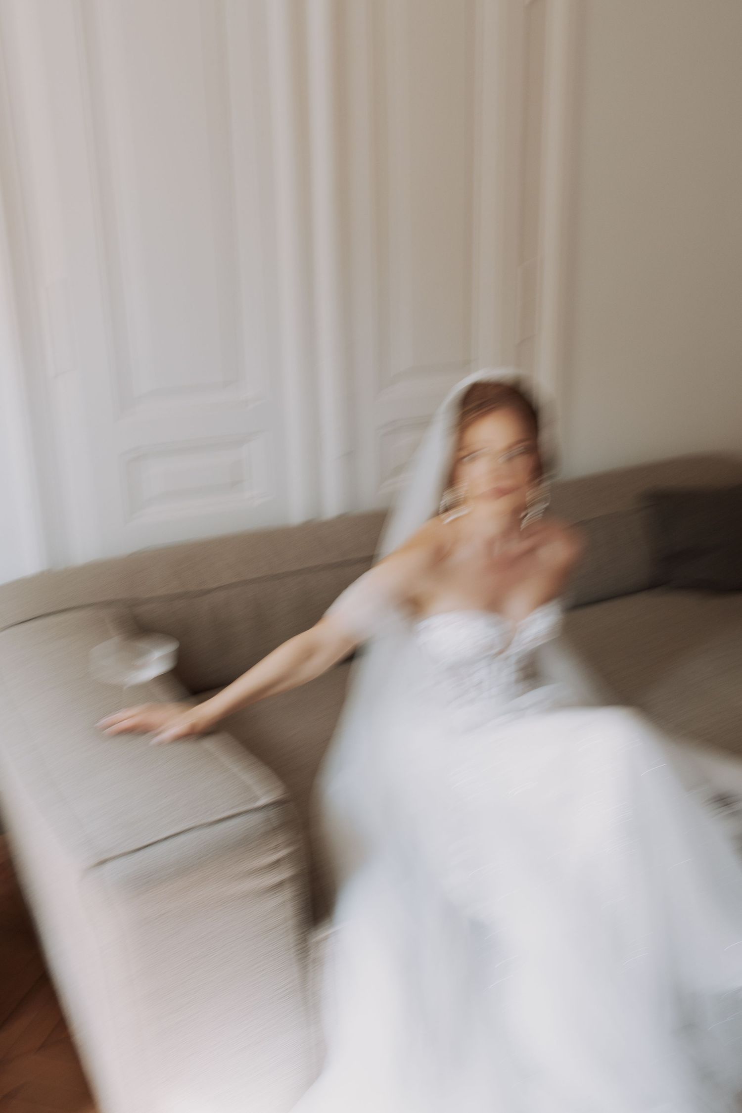 Motion blur sequence of person in white dress spinning on grey couch.