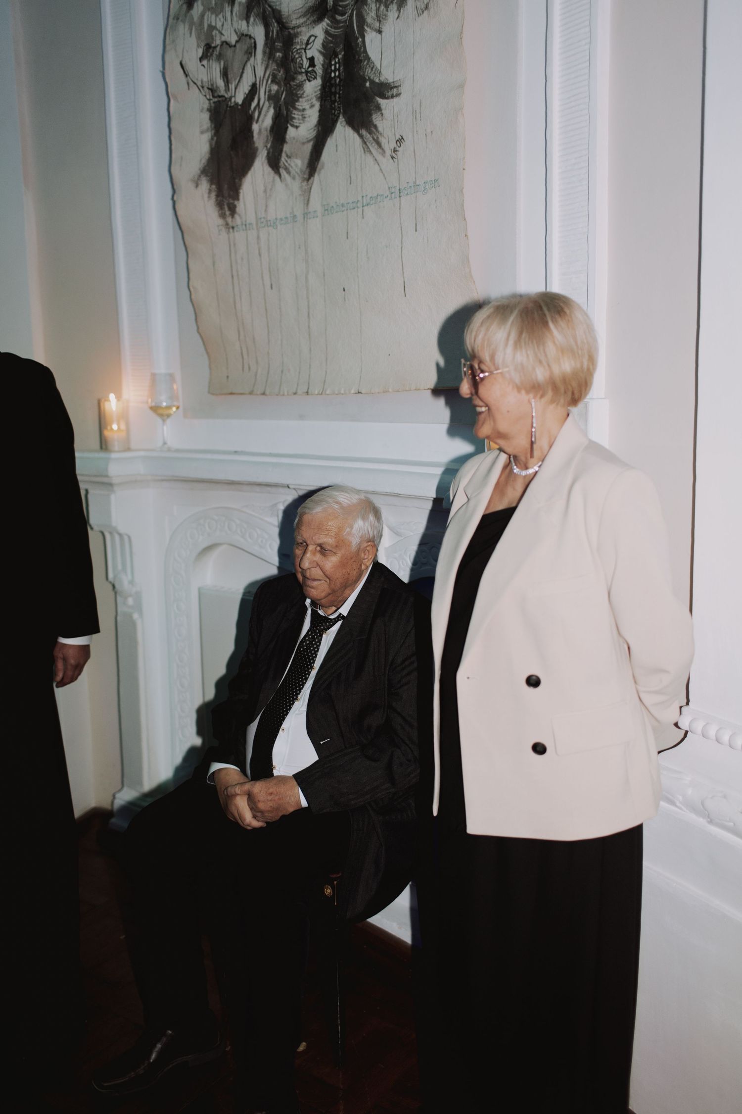 Wedding guests in formal attire conversing in a dimly lit venue corner.