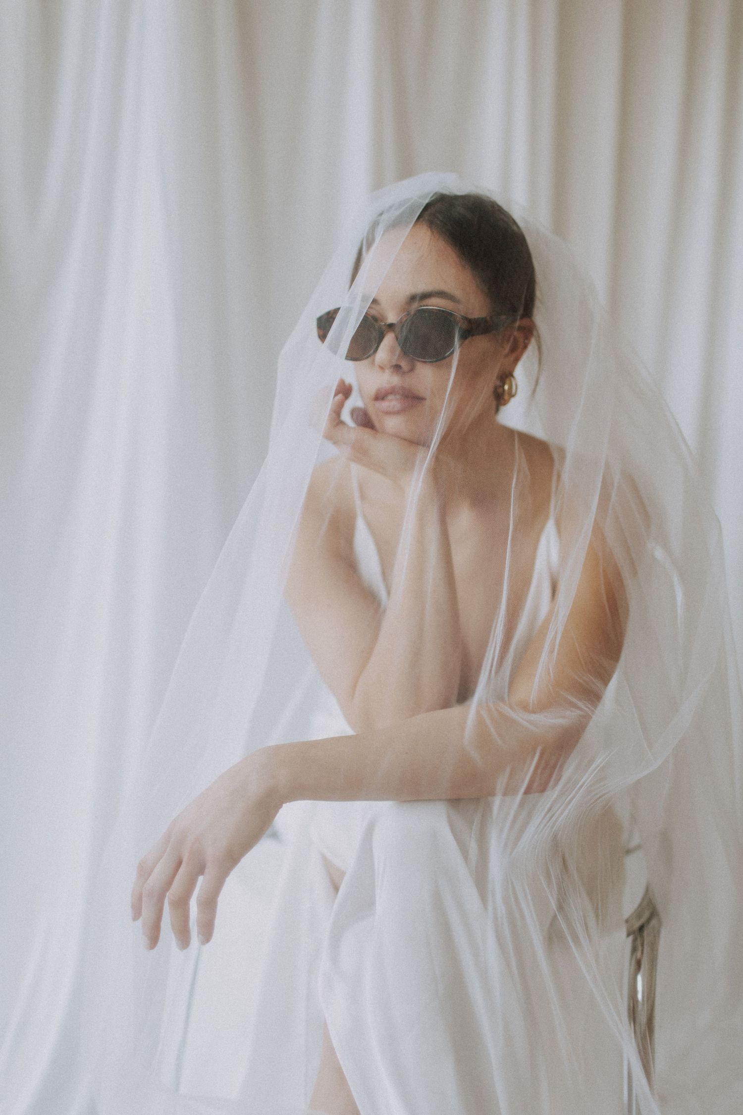 Dreamy bridal portraits with flowing veil against white curtain backdrop.