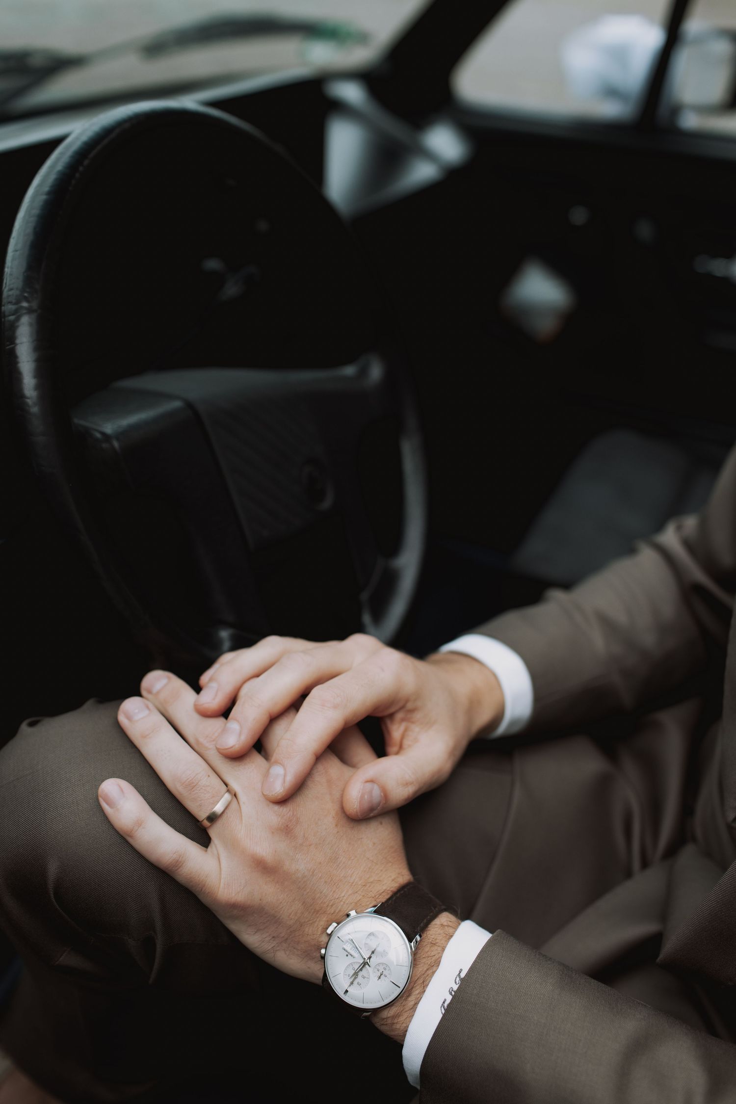 Close-up of hands with a wristwatch resting on a car's steering wheel.