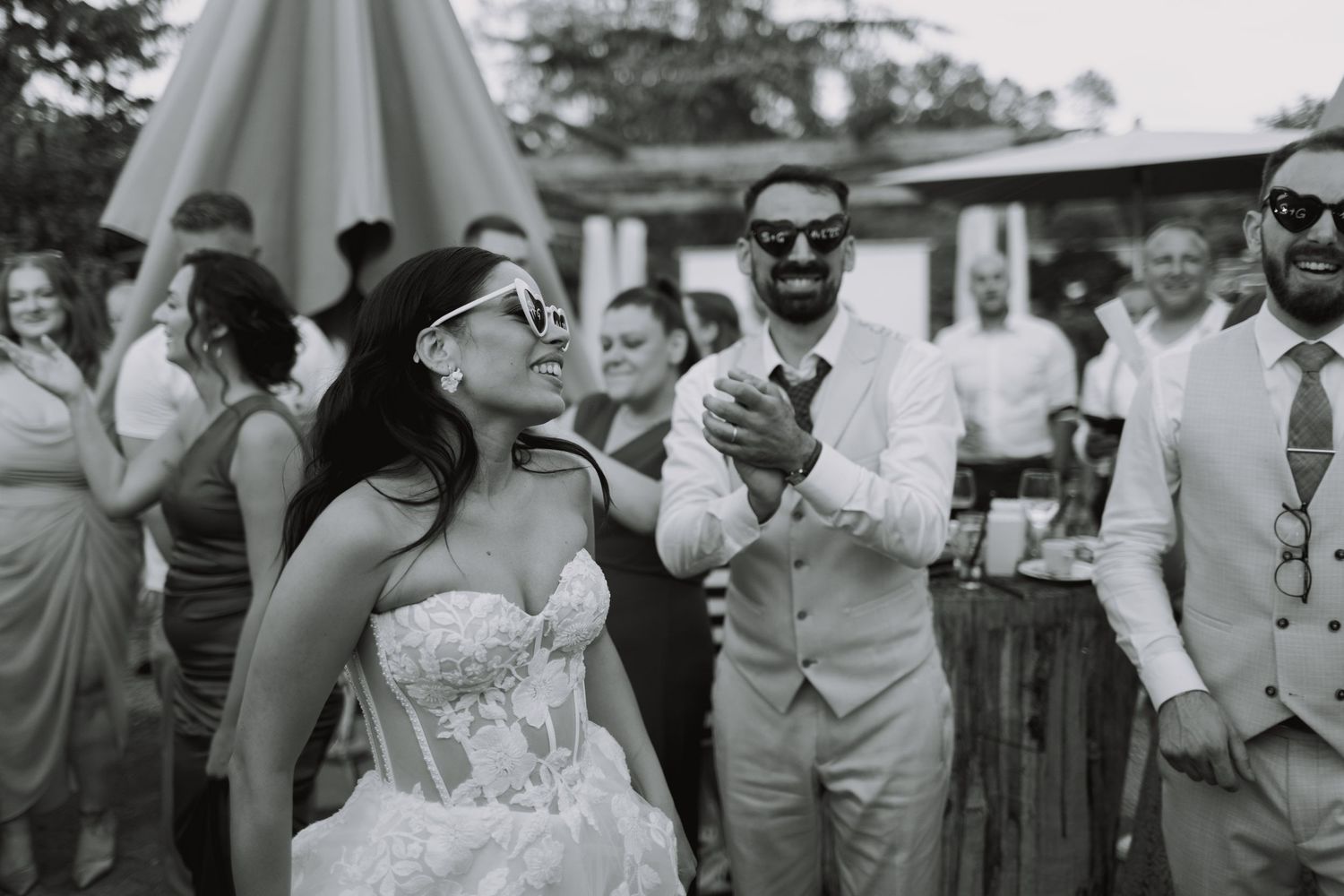 Wedding party in gray suits and dresses celebrating outdoors during a joyful reception moment.