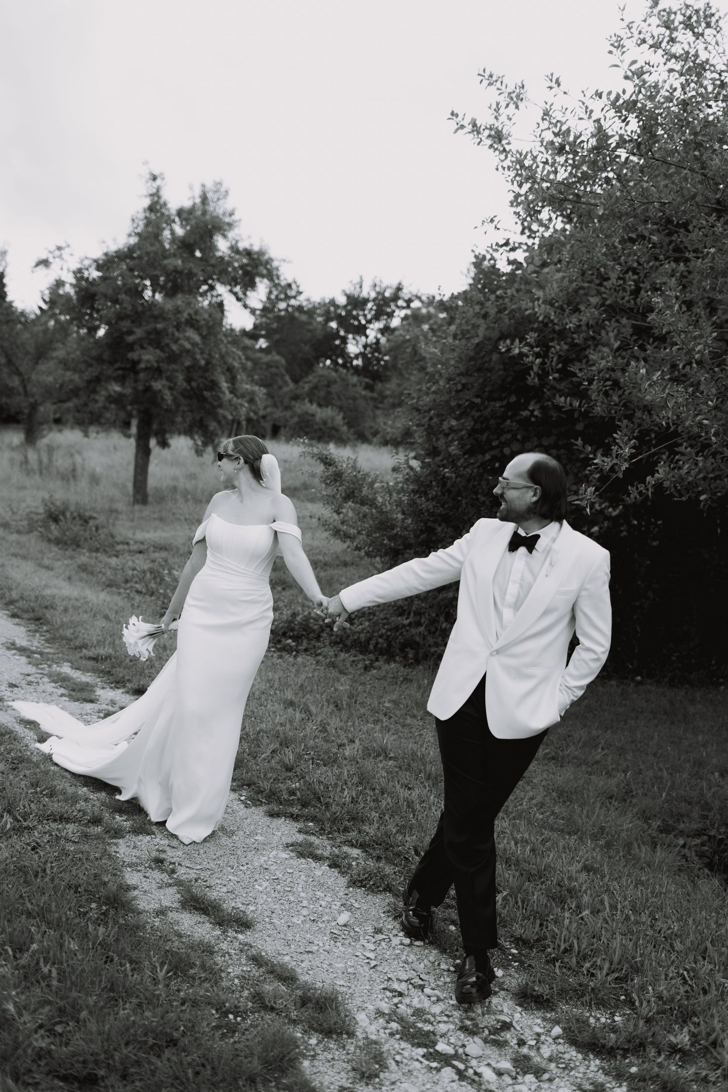 A sequence of black and white photos showing a couple in wedding attire playfully dancing in an orchard setting.