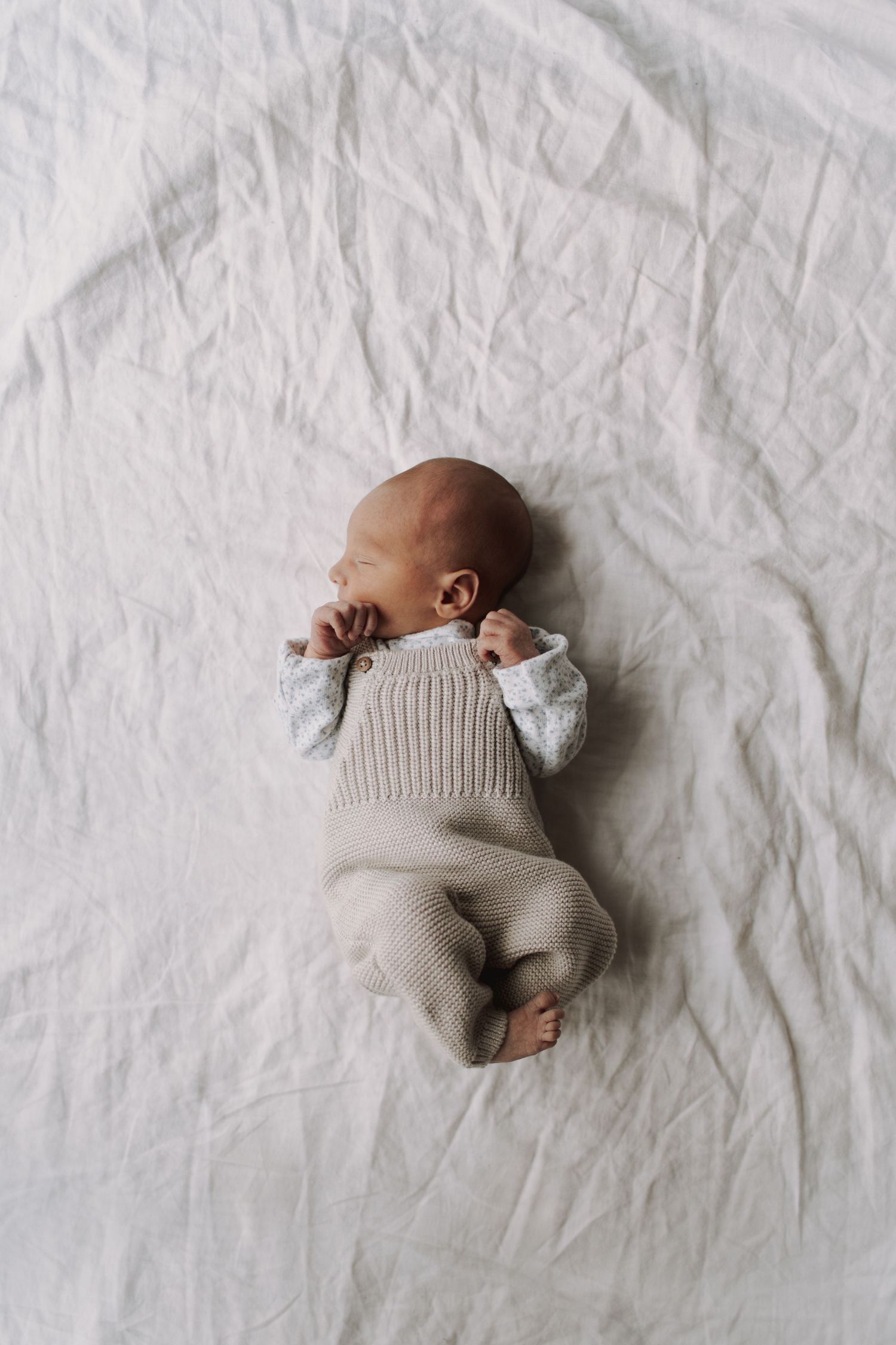 Overhead view of baby wearing knit sweater lying on white textured fabric.