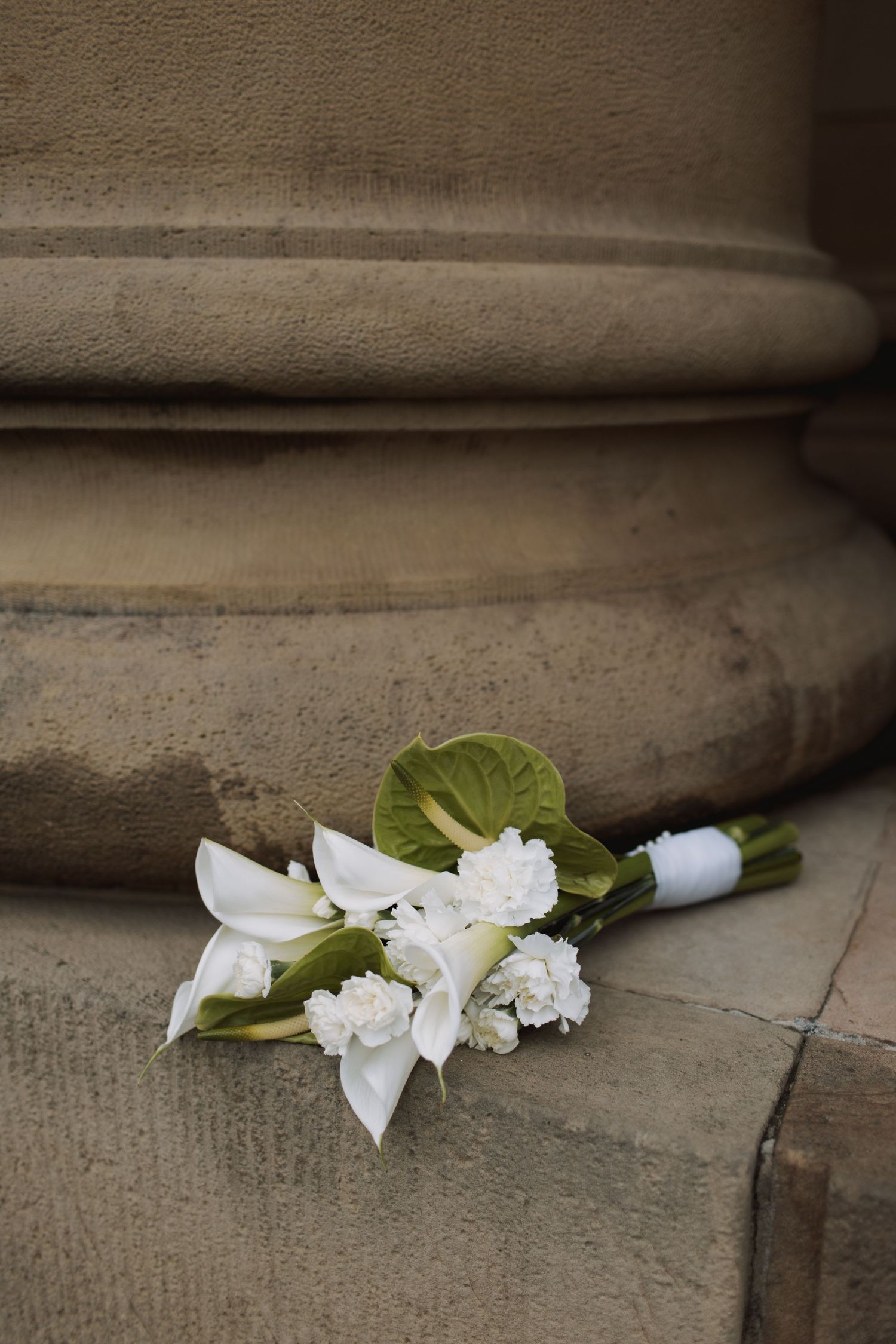 A white lily and rose bouquet rests against stone steps.