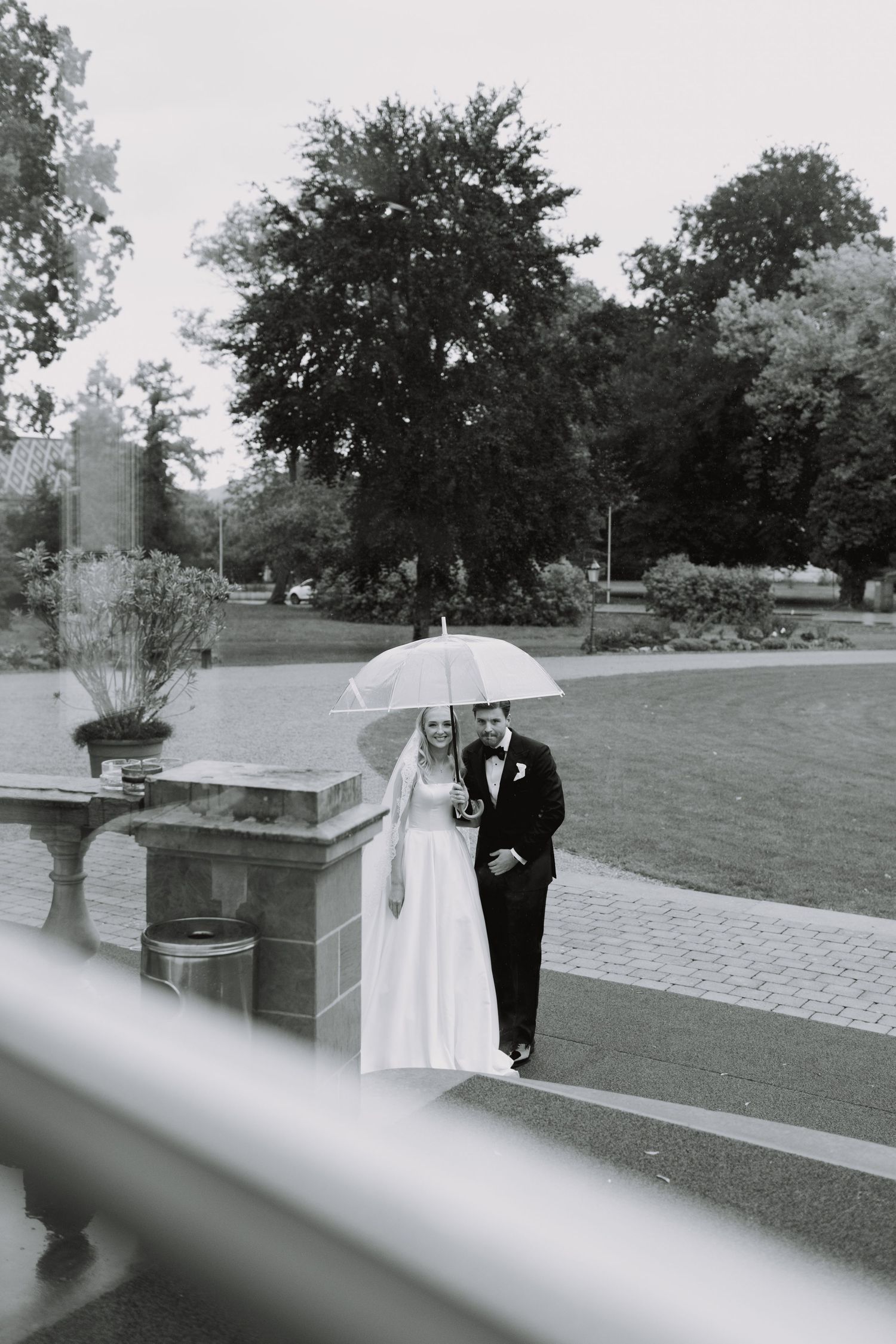 Black and white wedding photo of a couple walking through an outdoor garden setting.