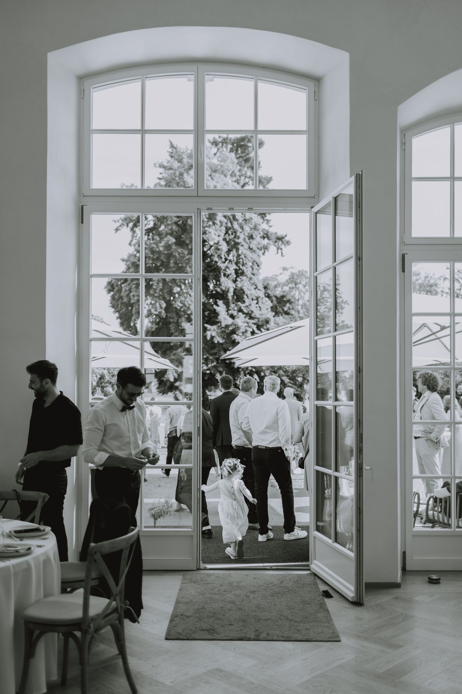 Modern event space with large arched windows and guests mingling in a bright interior.