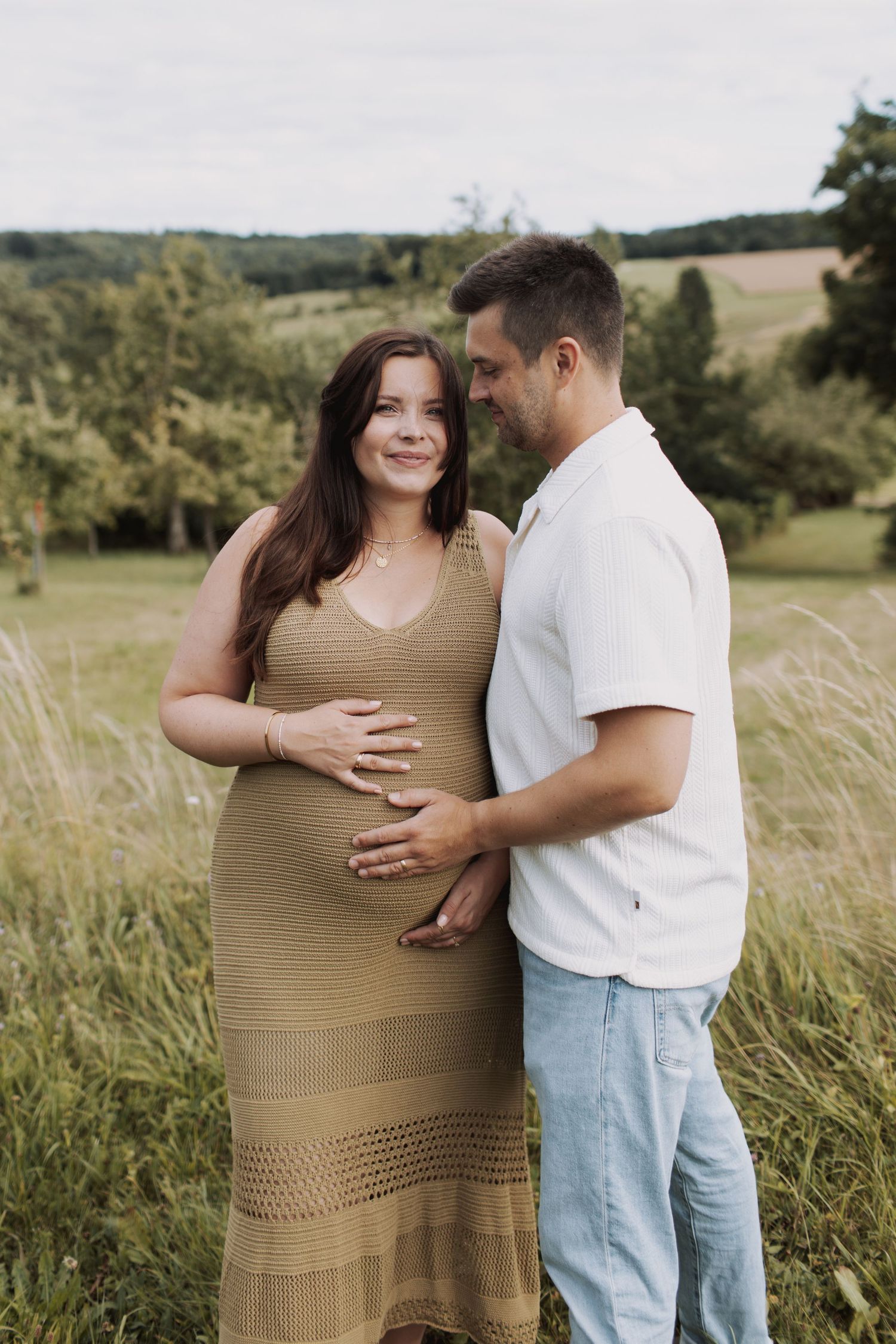 Intimate maternity photo session in a golden field with couple embracing and touching pregnant belly.