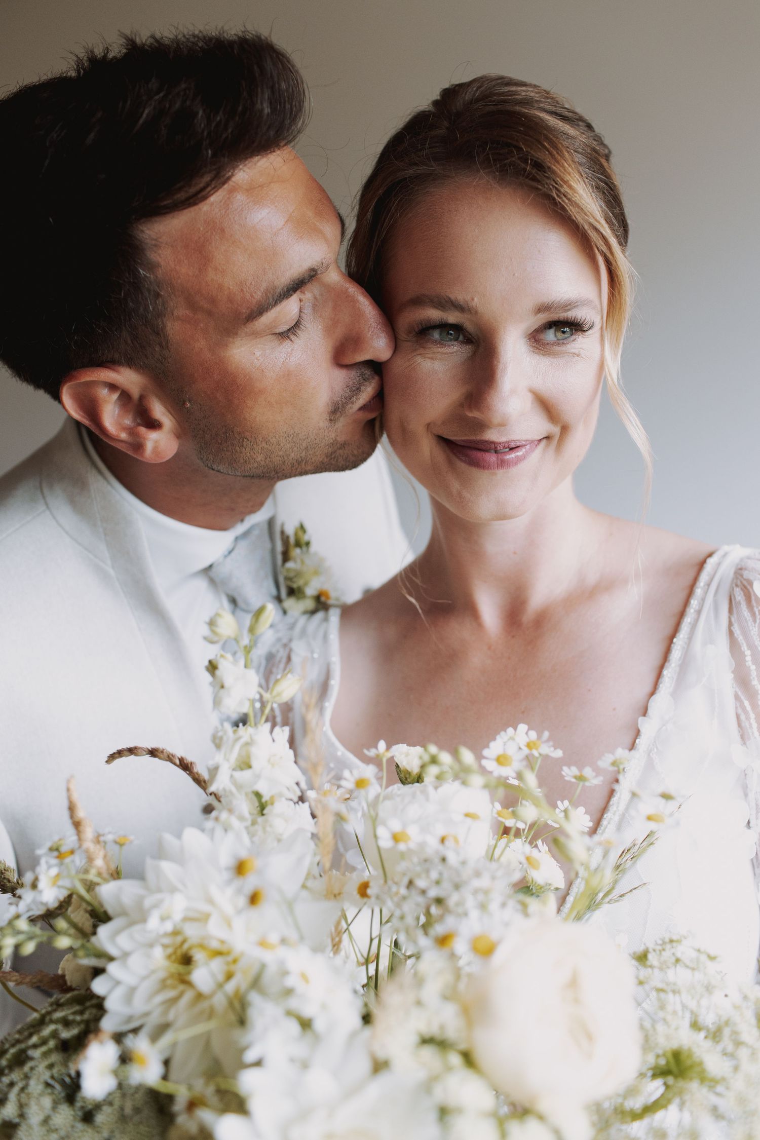 A romantic wedding photo series showing tender moments between a couple with a delicate white floral bouquet.