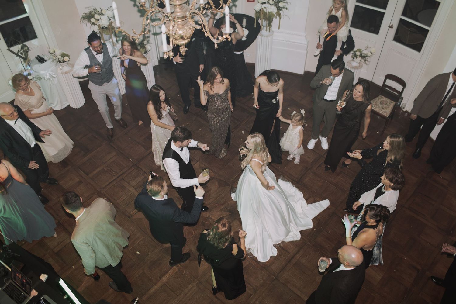 Overhead view of wedding guests mingling and dancing on a dark wooden floor.