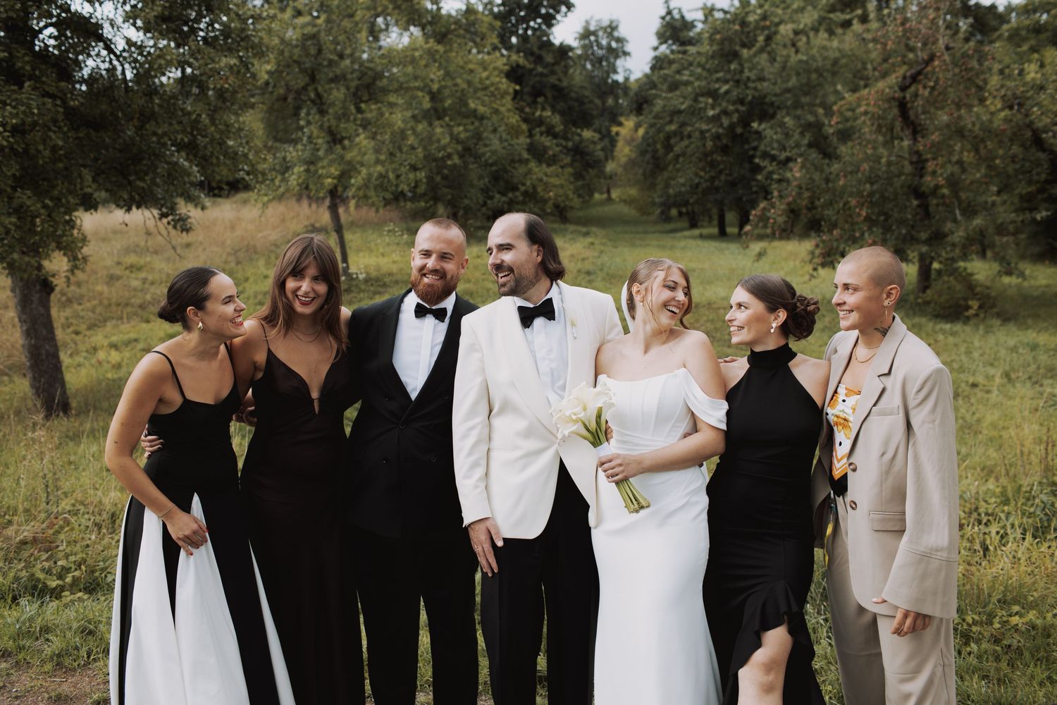Wedding party in formal attire gathered outdoors for group photos.