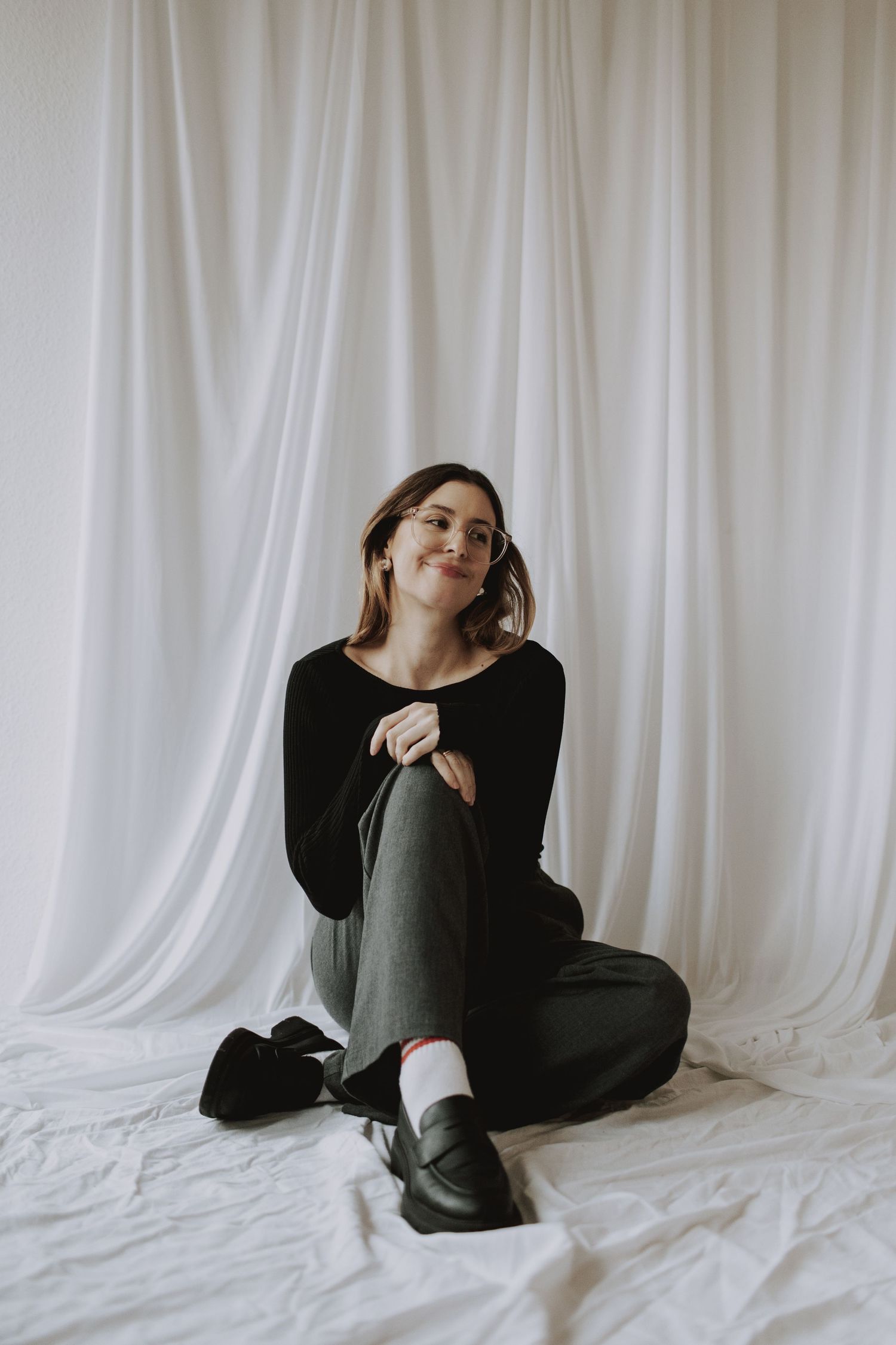 Figure in dark clothing poses expressively on white floor in studio setting.