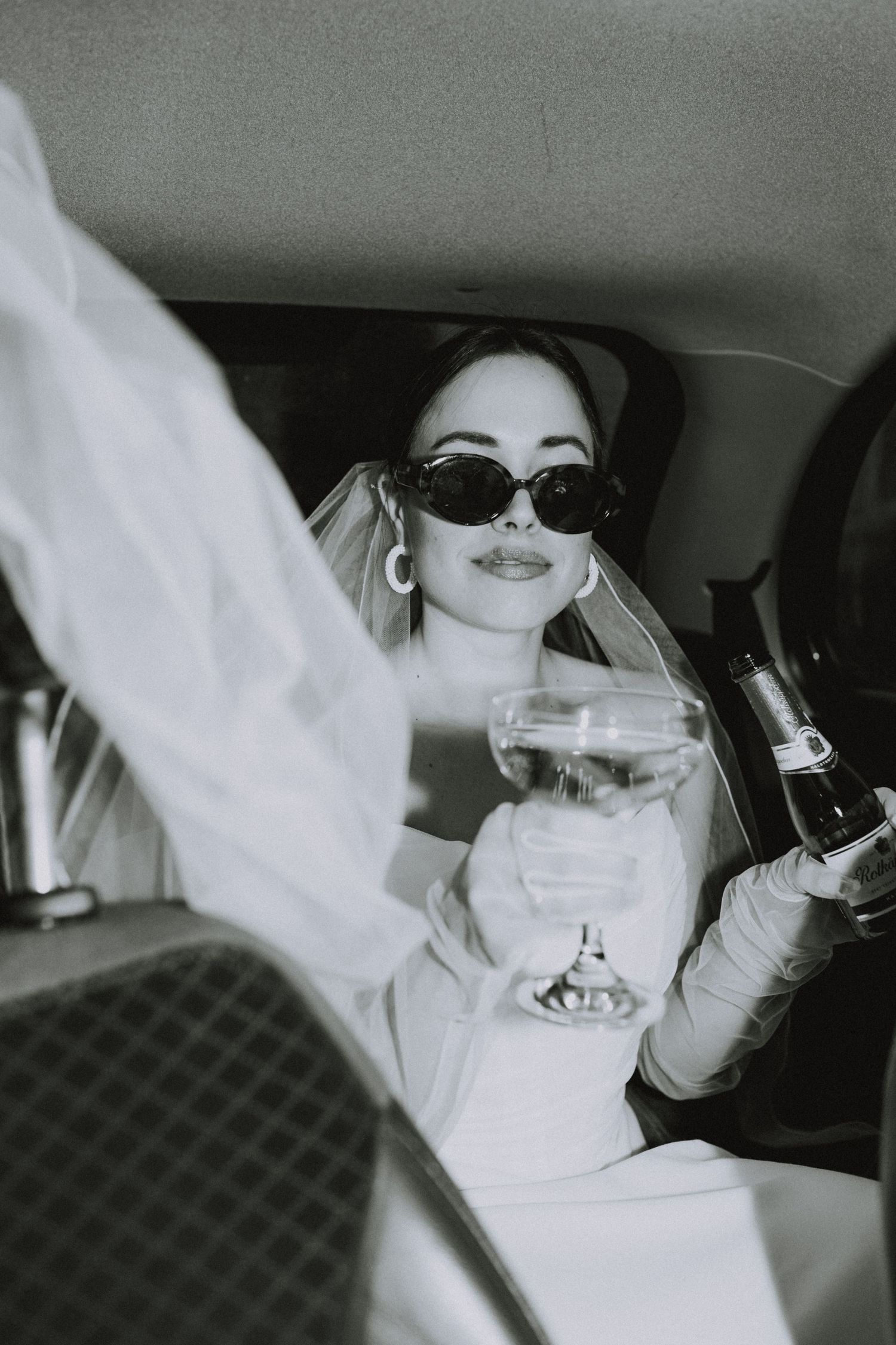 Black and white photos of someone in white outfit posing playfully inside a car.