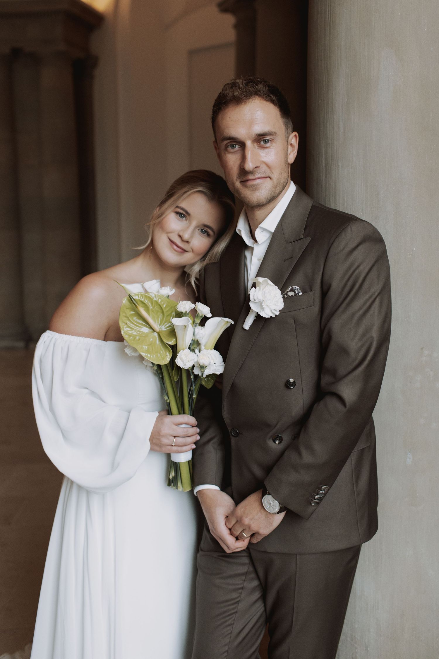 Wedding portrait with couple holding calla lily bouquet against stone columns.