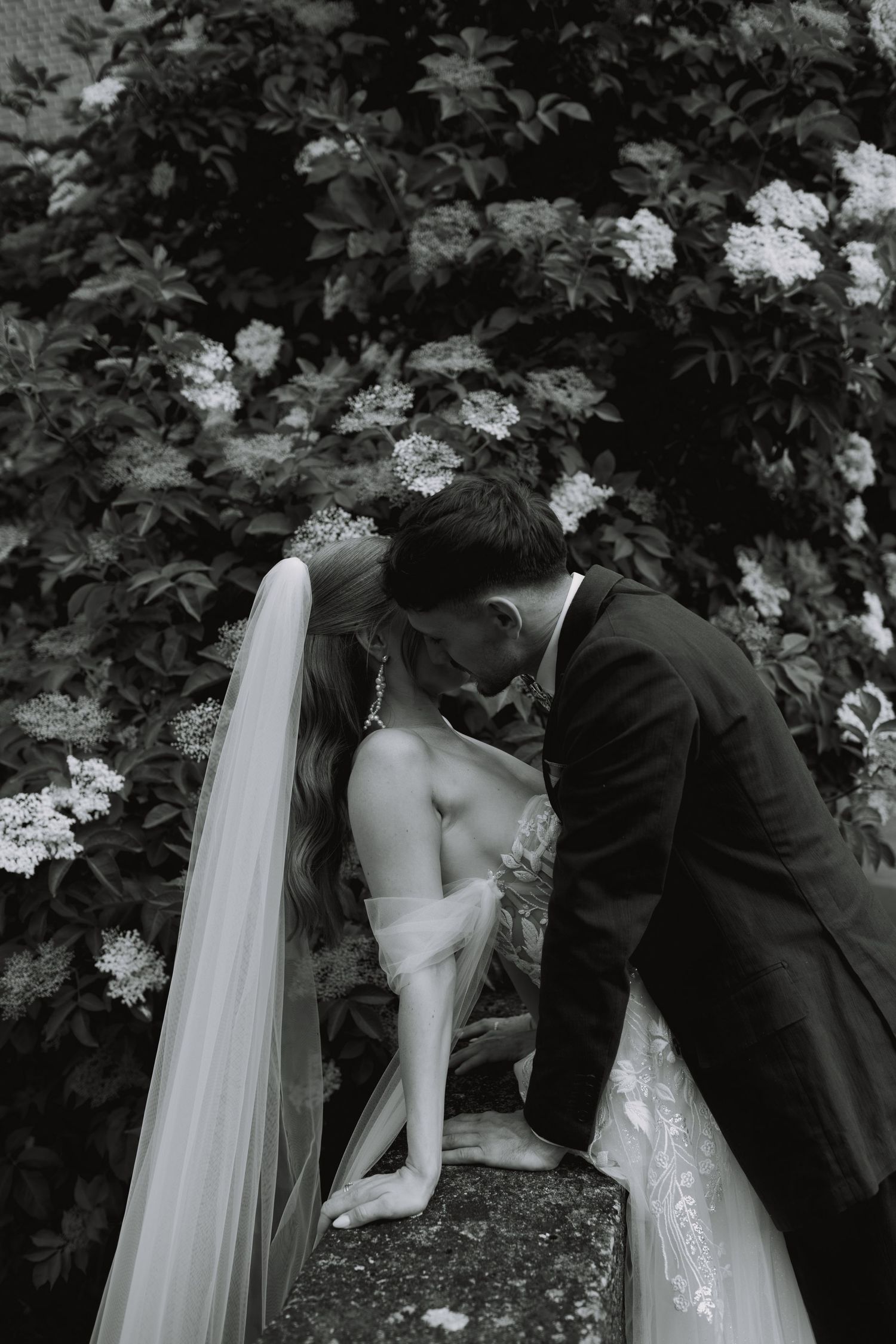 A romantic black and white wedding photo sequence showing a couple embracing near flowering bushes.