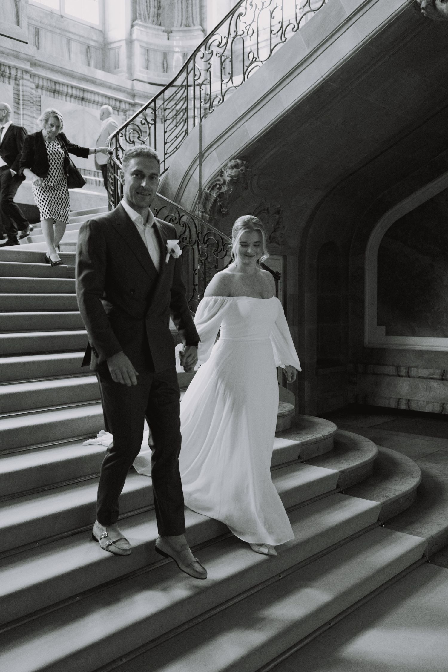 Wedding couple descending ornate staircase in formal attire.