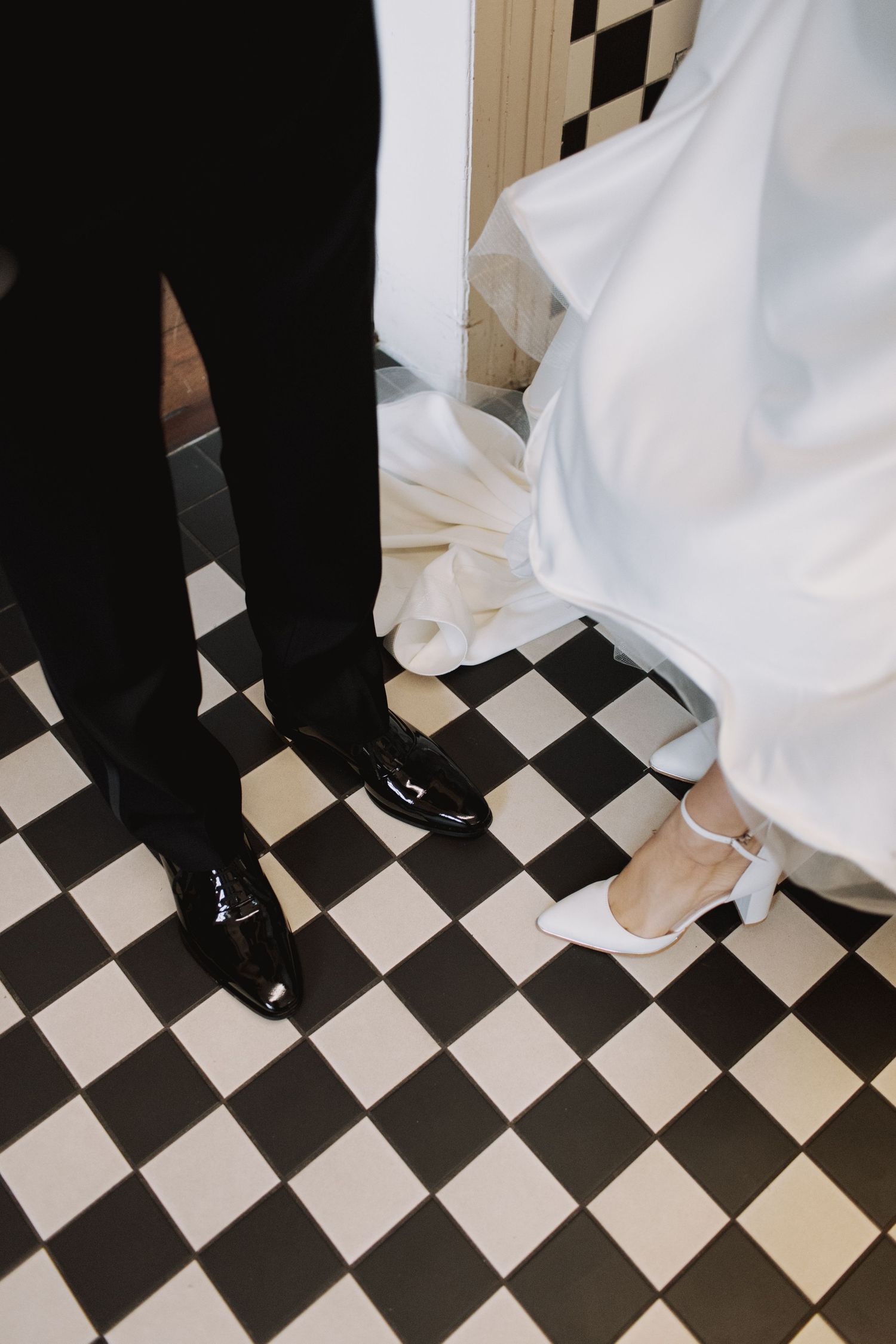 Wedding shoes on a black and white checkered floor with dress and suit details.