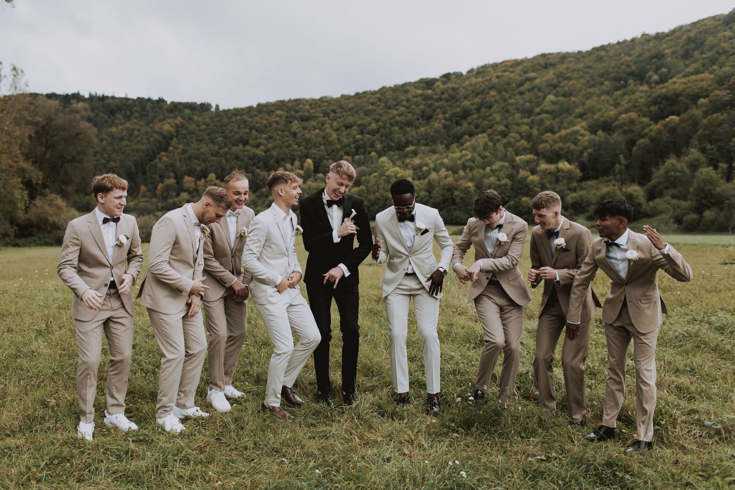 Groomsmen in light colored suits posing playfully outdoors with mountain scenery.