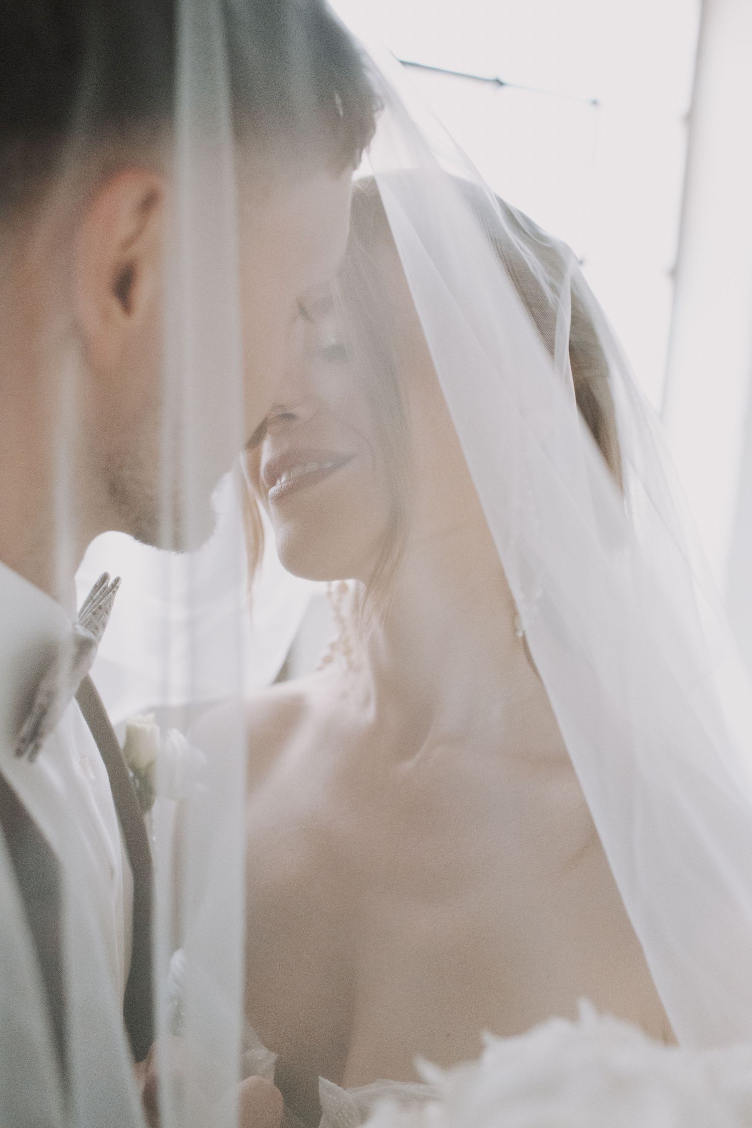 An intimate moment captured through a sheer bridal veil in soft lighting.