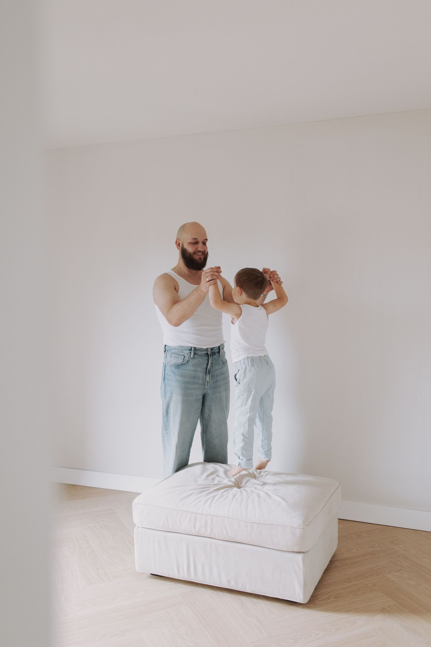 Playful sequence of two people jumping and interacting on a white couch against a minimalist background.