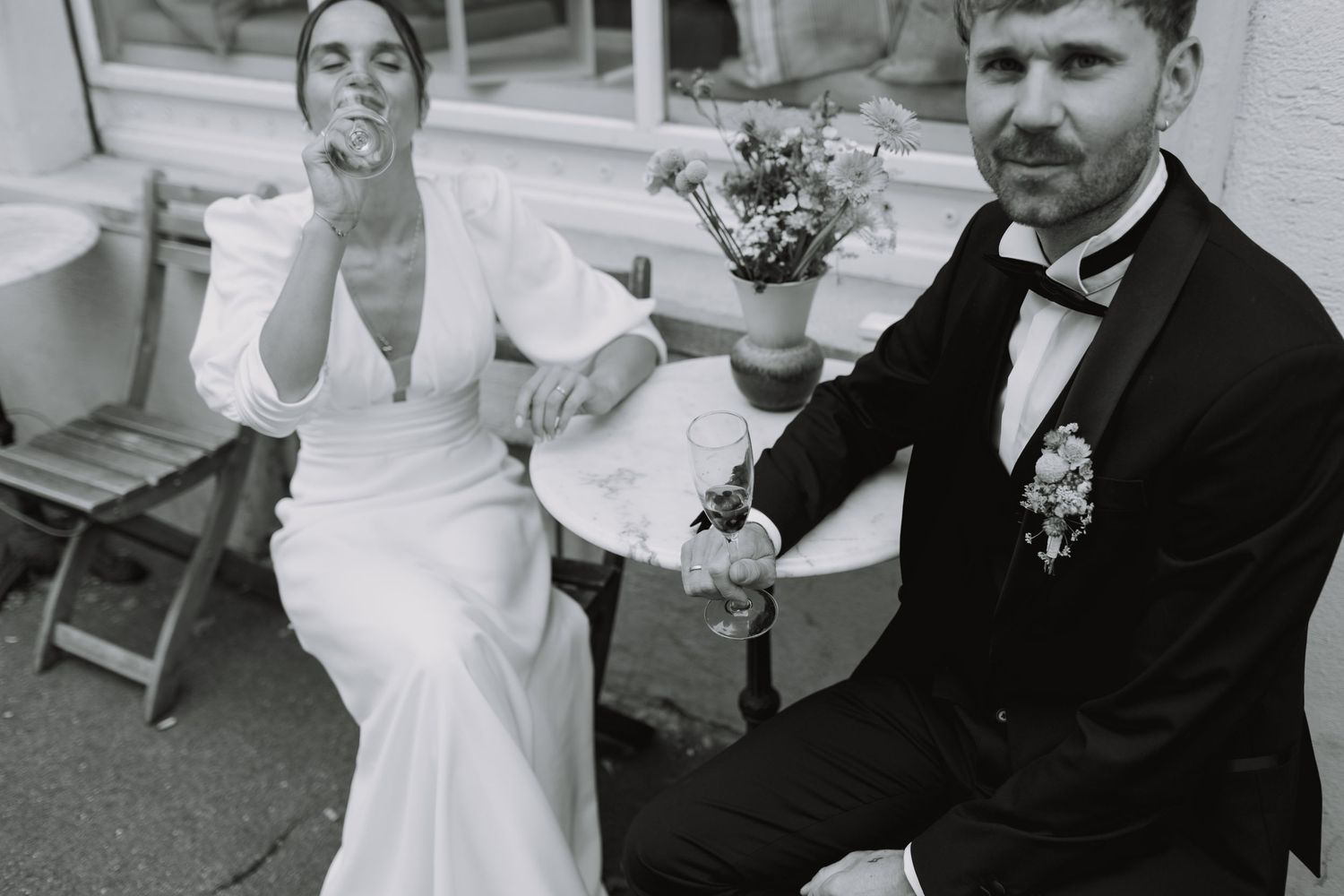 Black and white photo of a bride and groom sitting outdoors at their wedding celebration.
