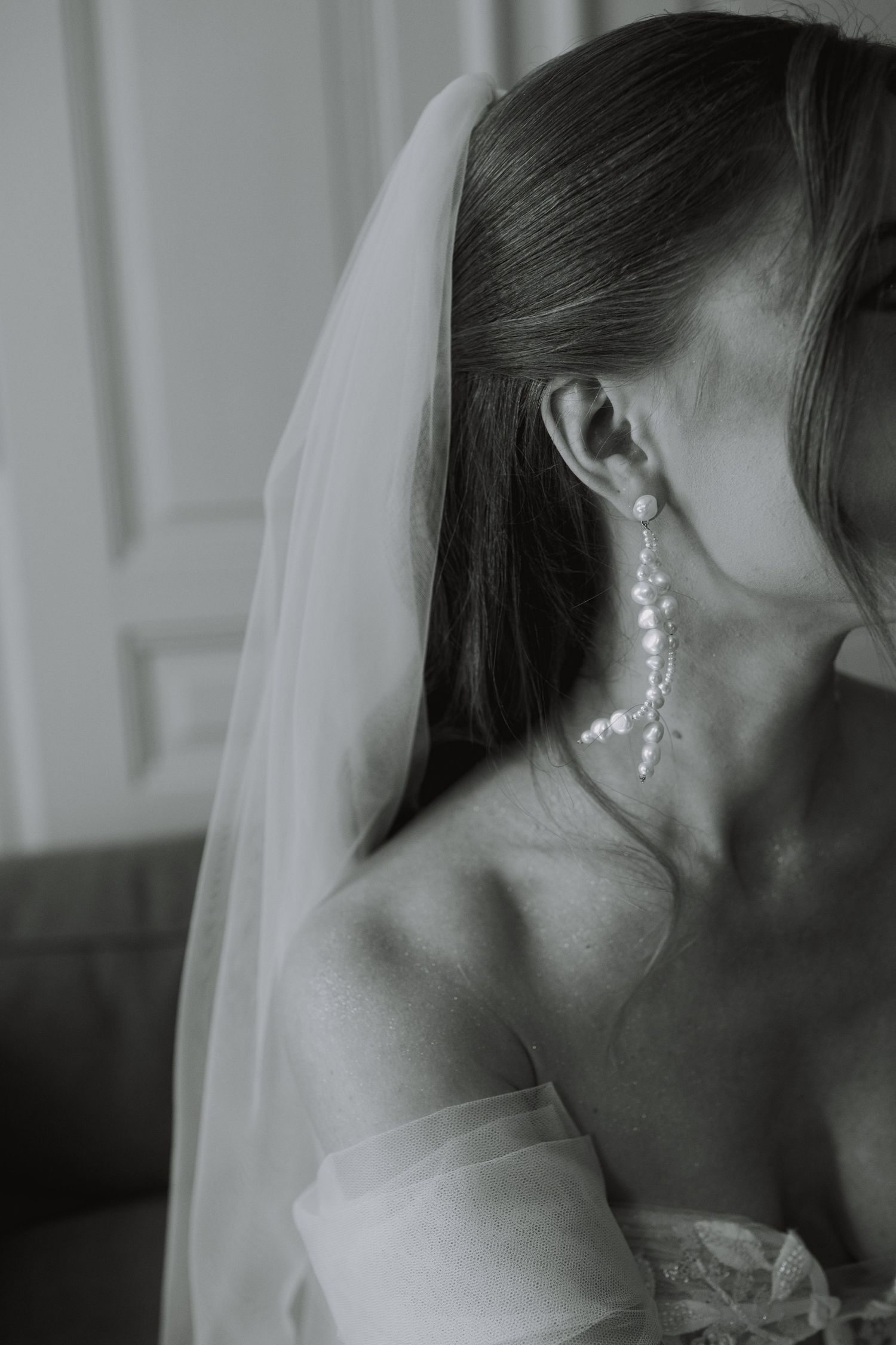 Close-up shot of a bride wearing elegant dangling pearl earrings and a flowing veil.
