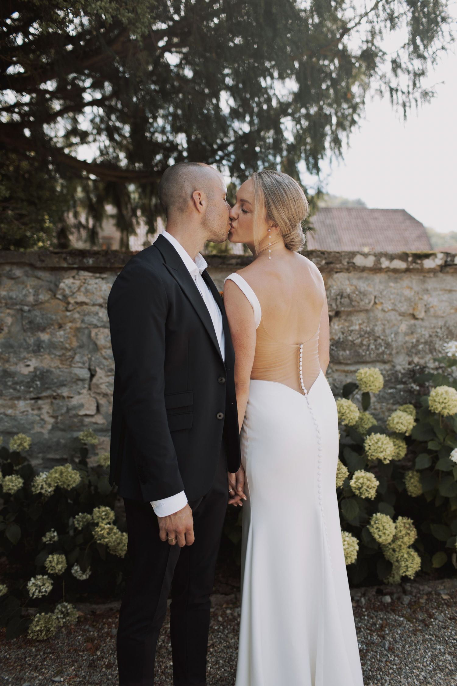Elegant wedding couple in formal attire sharing romantic moments against a stone wall backdrop.
