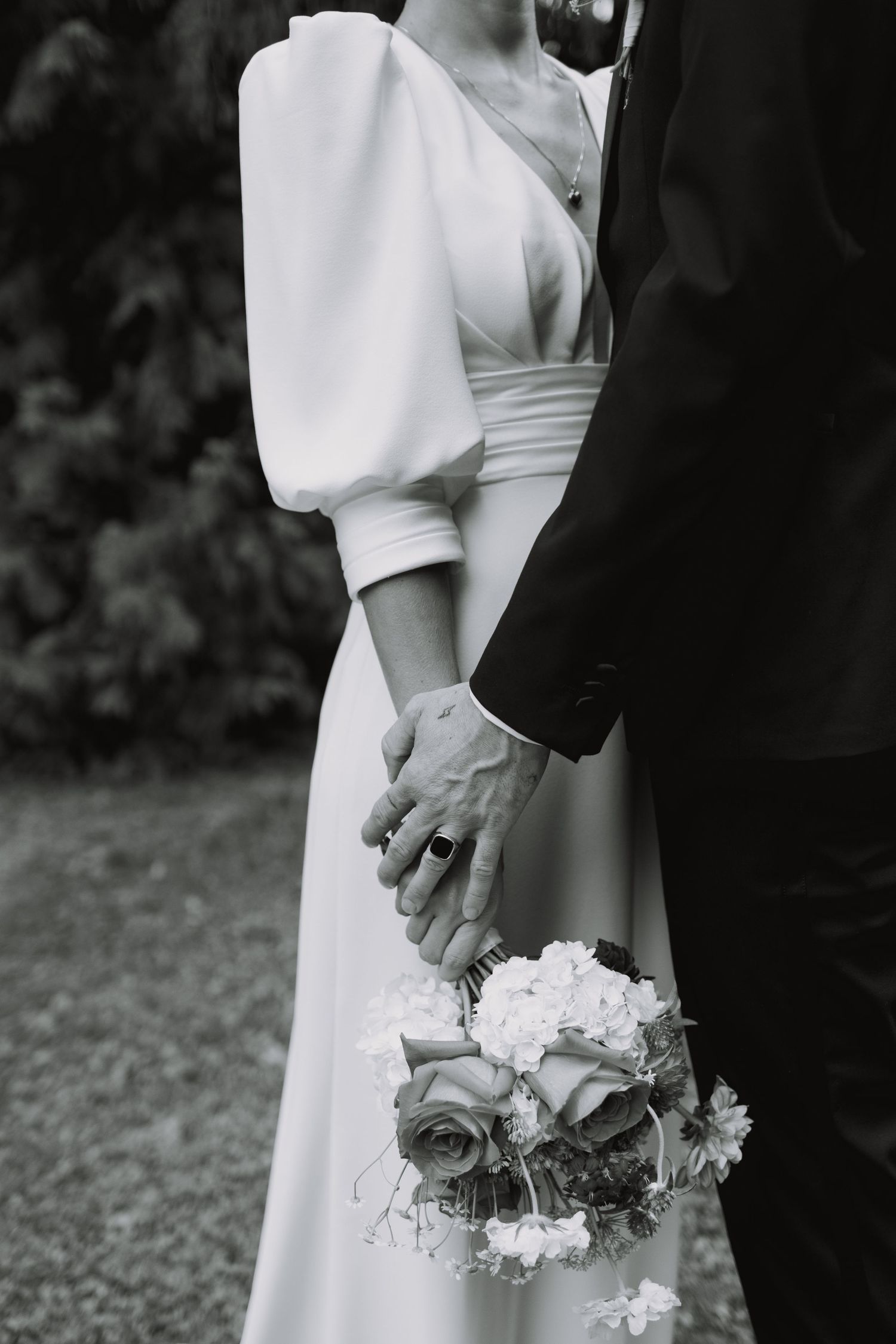 Close-up of wedding couple holding hands with floral bouquet details.