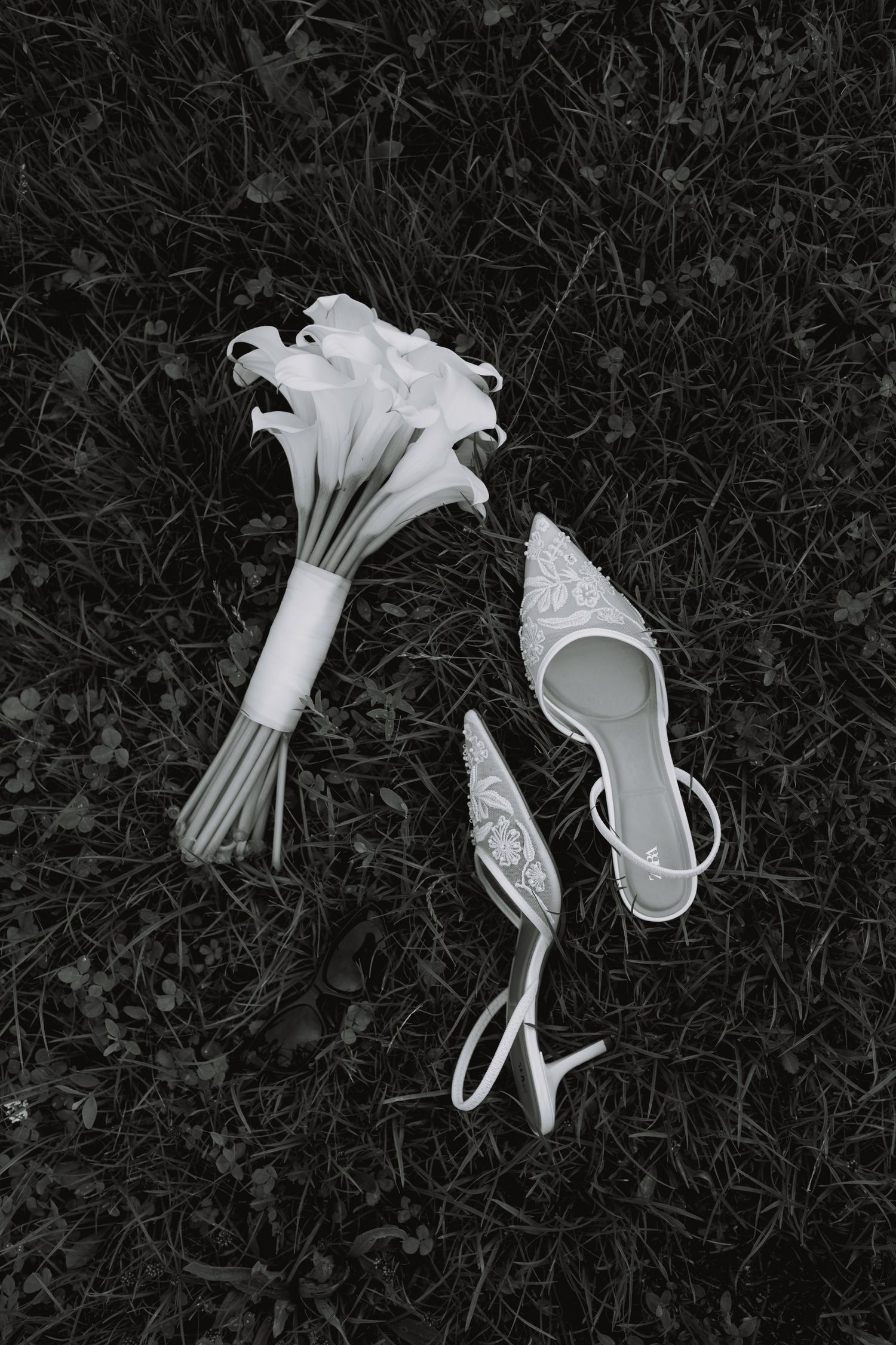 White wedding bouquet and bridal shoes laid on dark grass.
