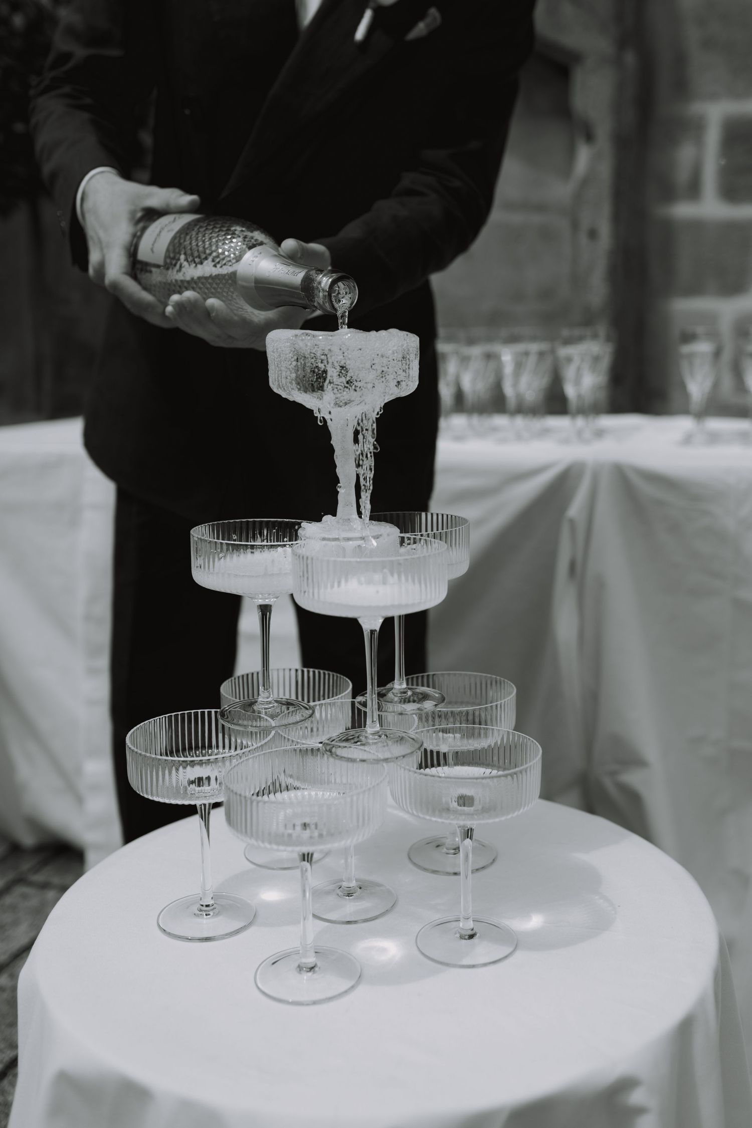 Champagne being poured into a tower of vintage coupe glasses at an elegant wedding reception.