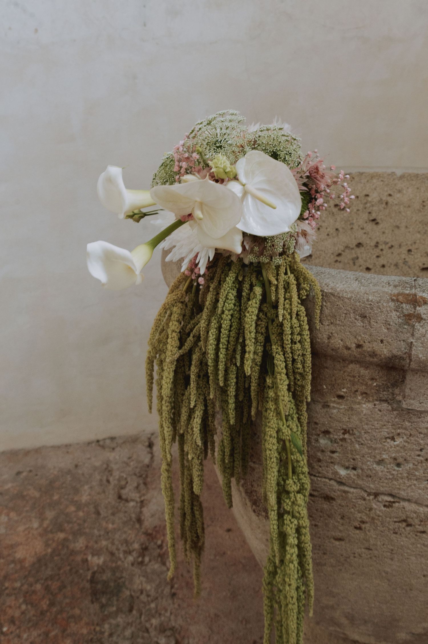 Decorative floral arrangement with cascading green amaranthus and white calla lilies.