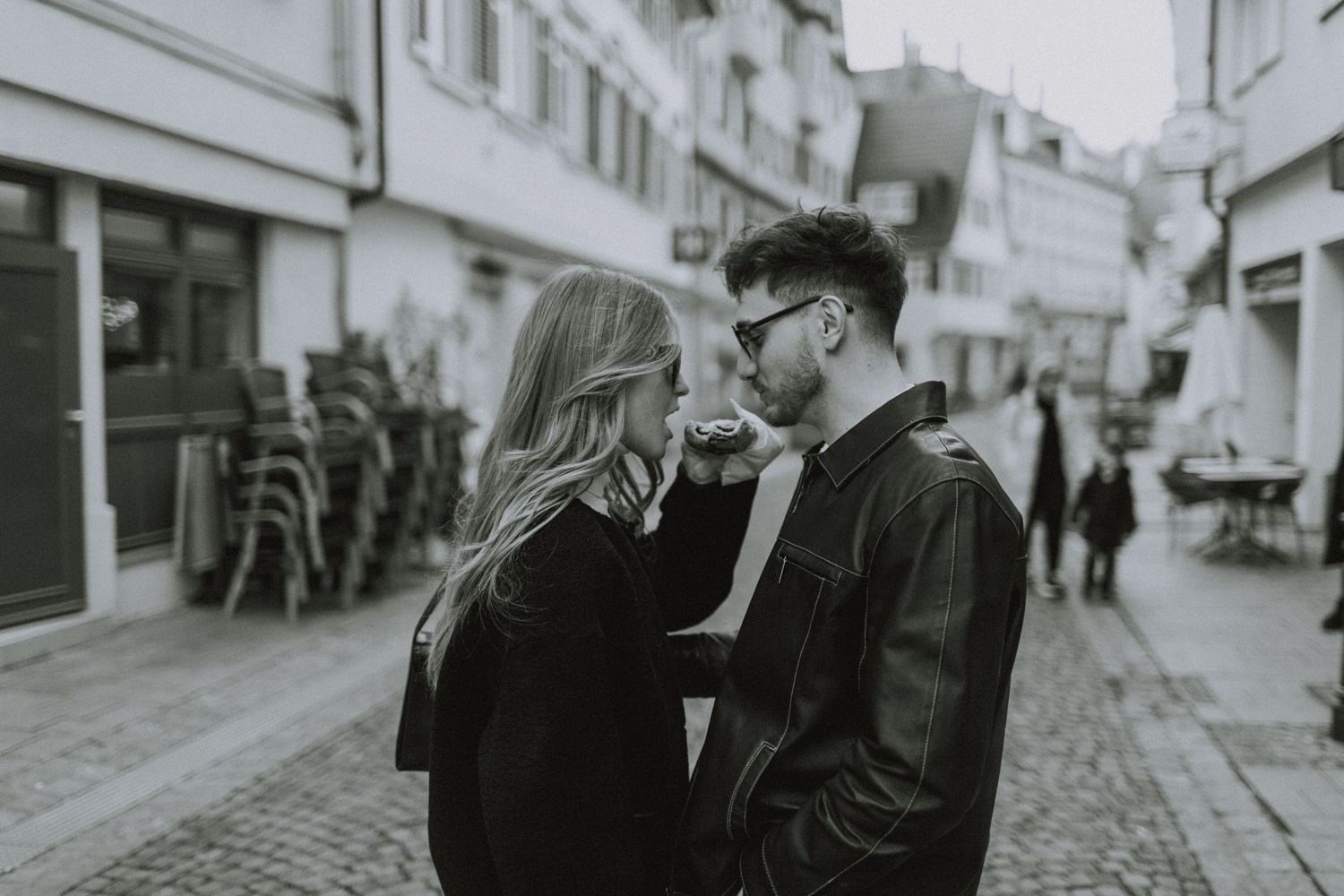 A black and white street photo of a couple in winter clothing on a cobblestone street.