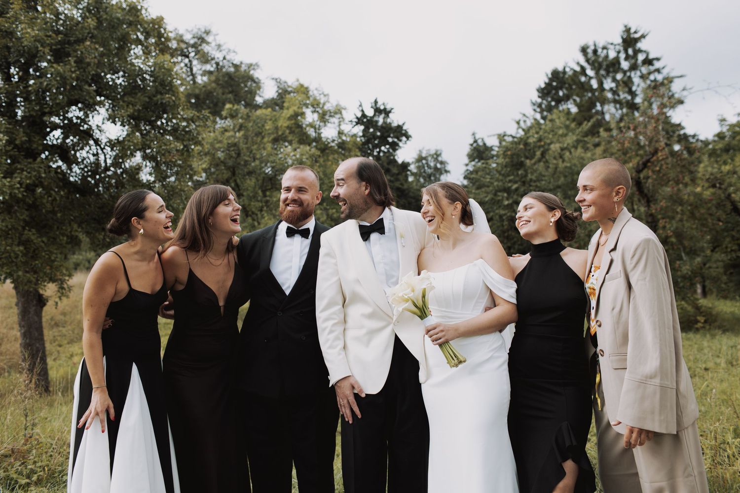Wedding party in black and white attire posing together outdoors.