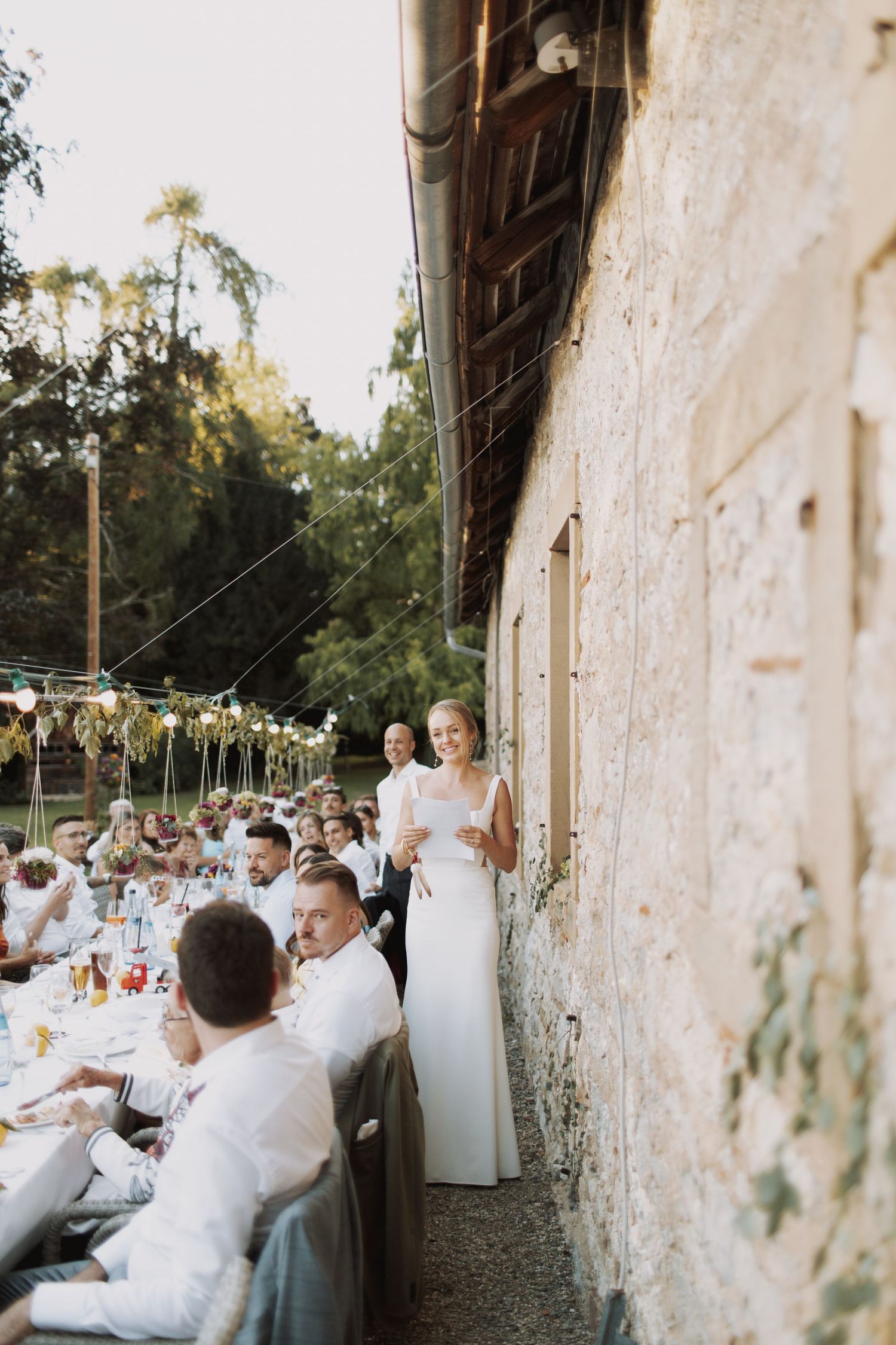 Wedding reception dinner setup along rustic stone walls with guests seated at long tables.