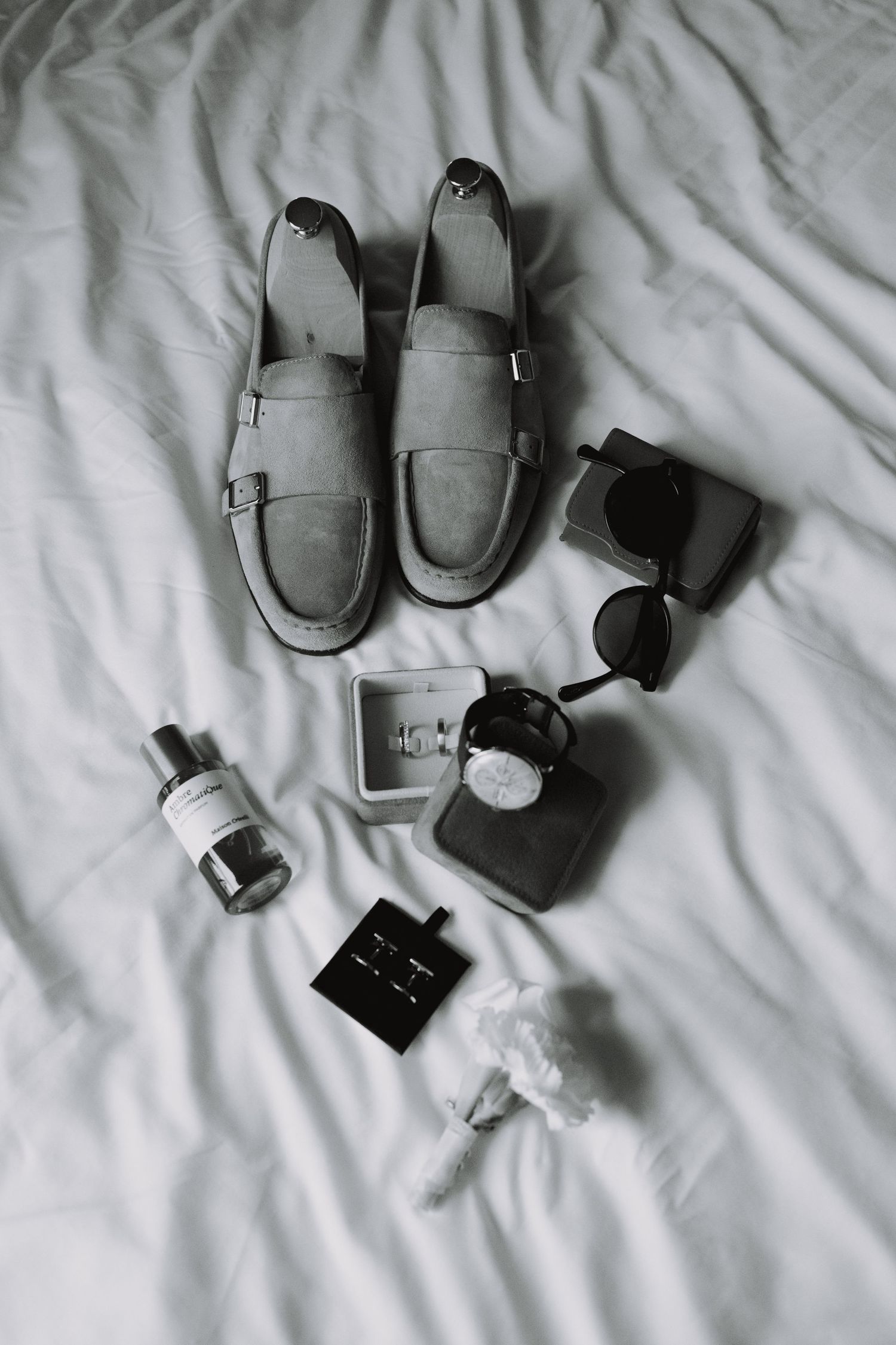 Flat lay of gray loafers, perfume bottles and accessories on white bedding.
