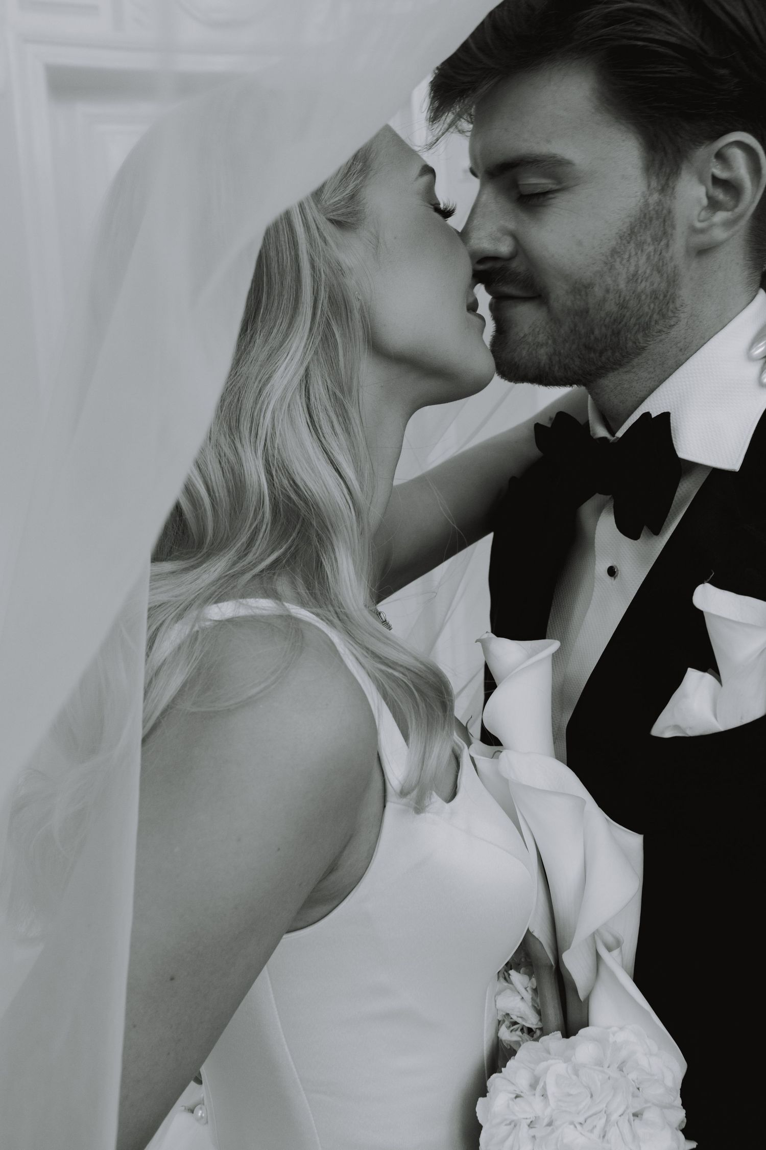 A romantic wedding moment captured in black and white under a flowing veil.
