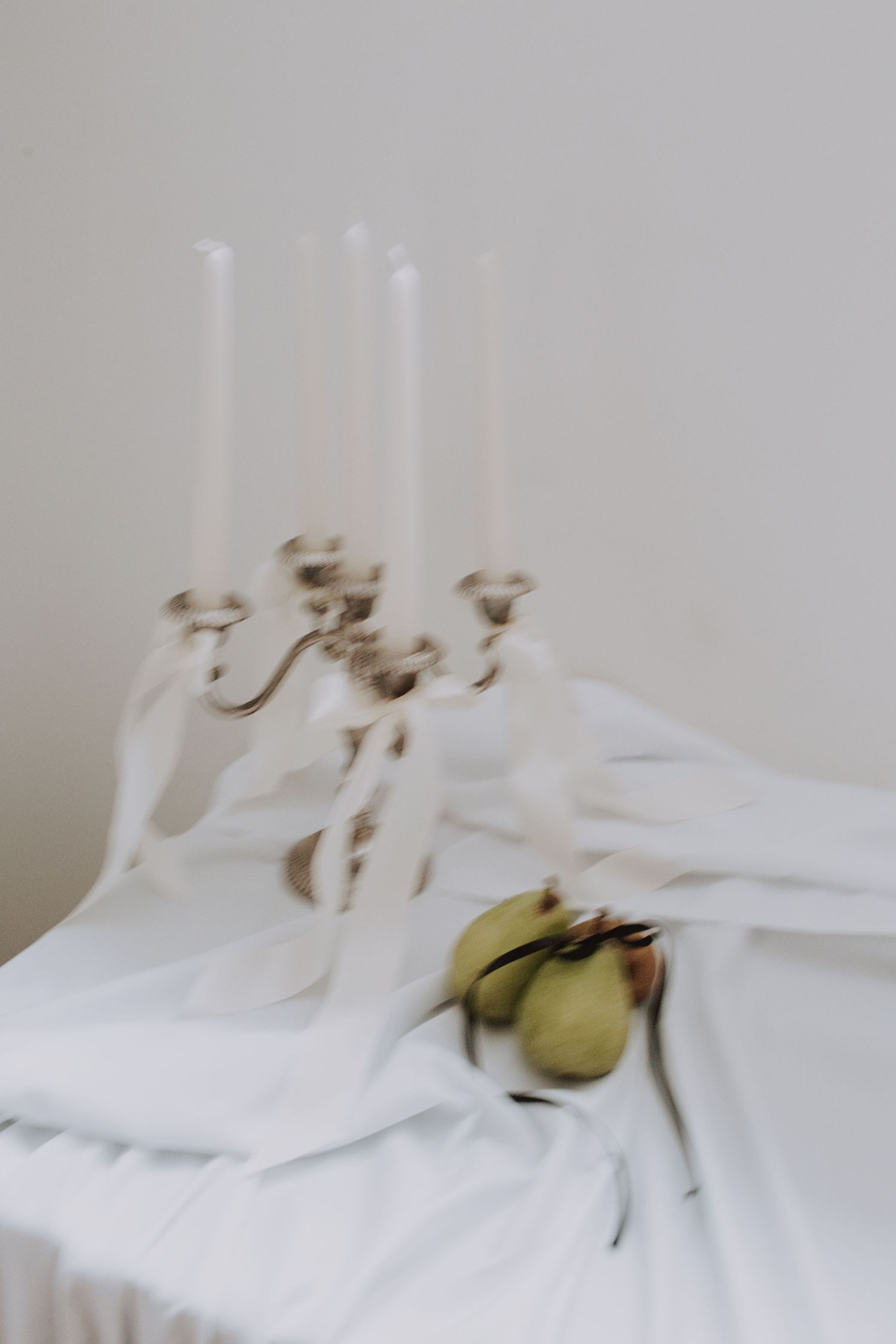 White candles and pears on white tablecloth with soft focus.