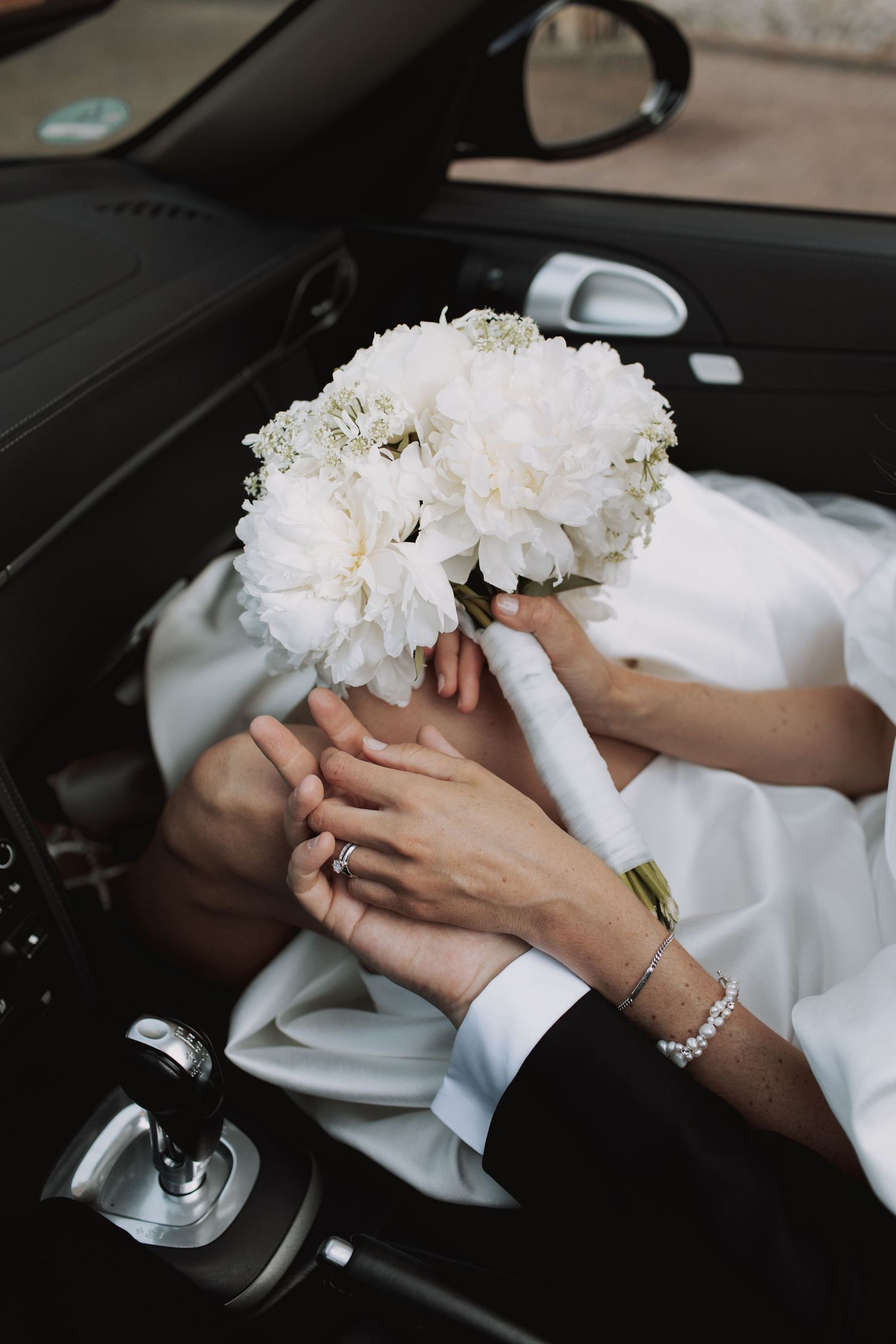 Intimate moment captured with hands holding a white floral bouquet against formal attire.