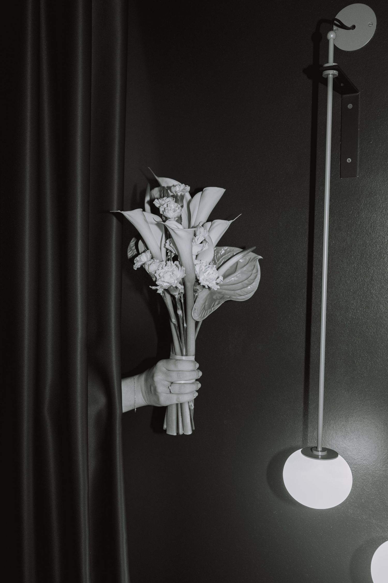 Hand holding a bouquet of white flowers against dark background with modern wall sconce.