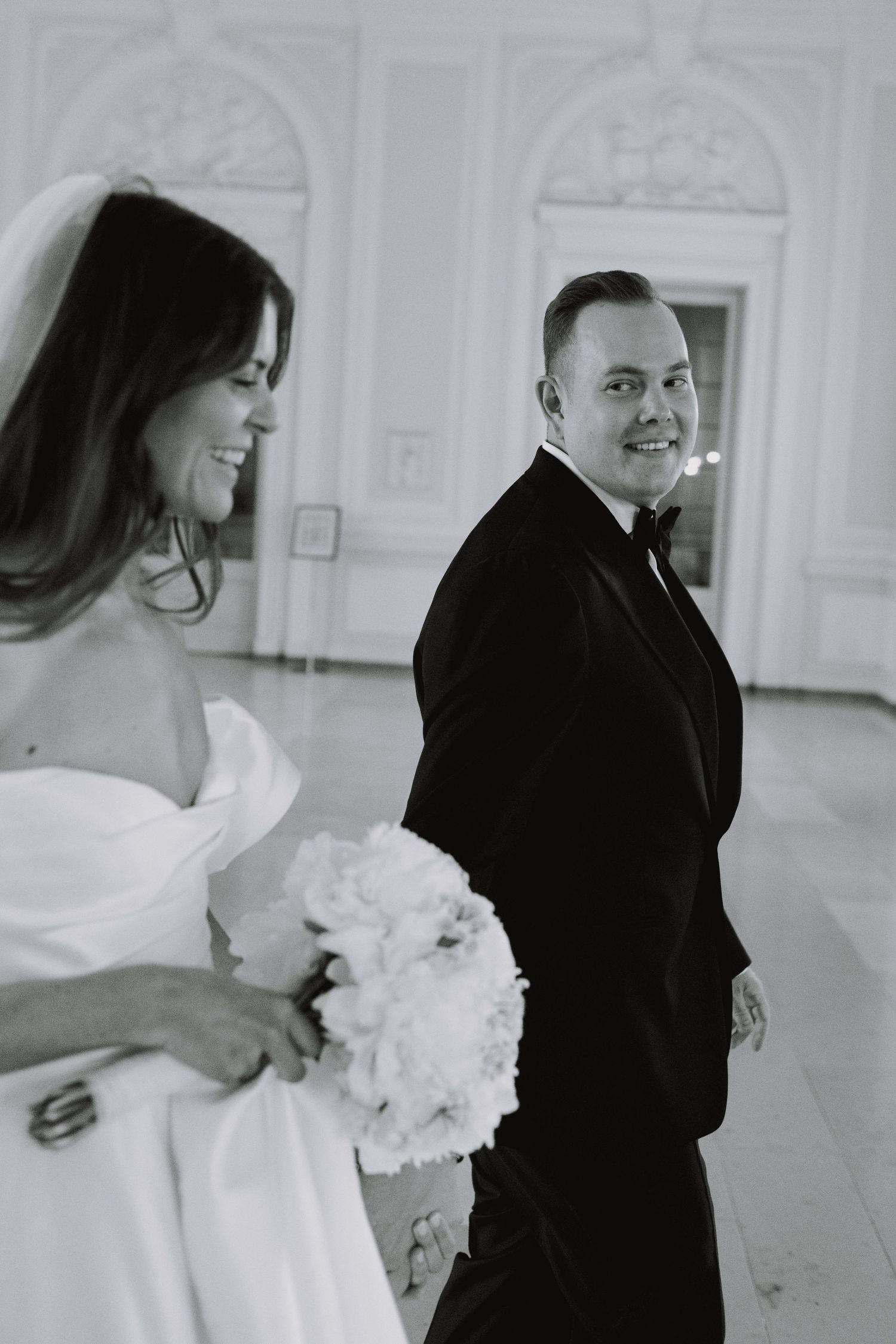 Black and white candid wedding moment in an elegant white room with classic architecture.