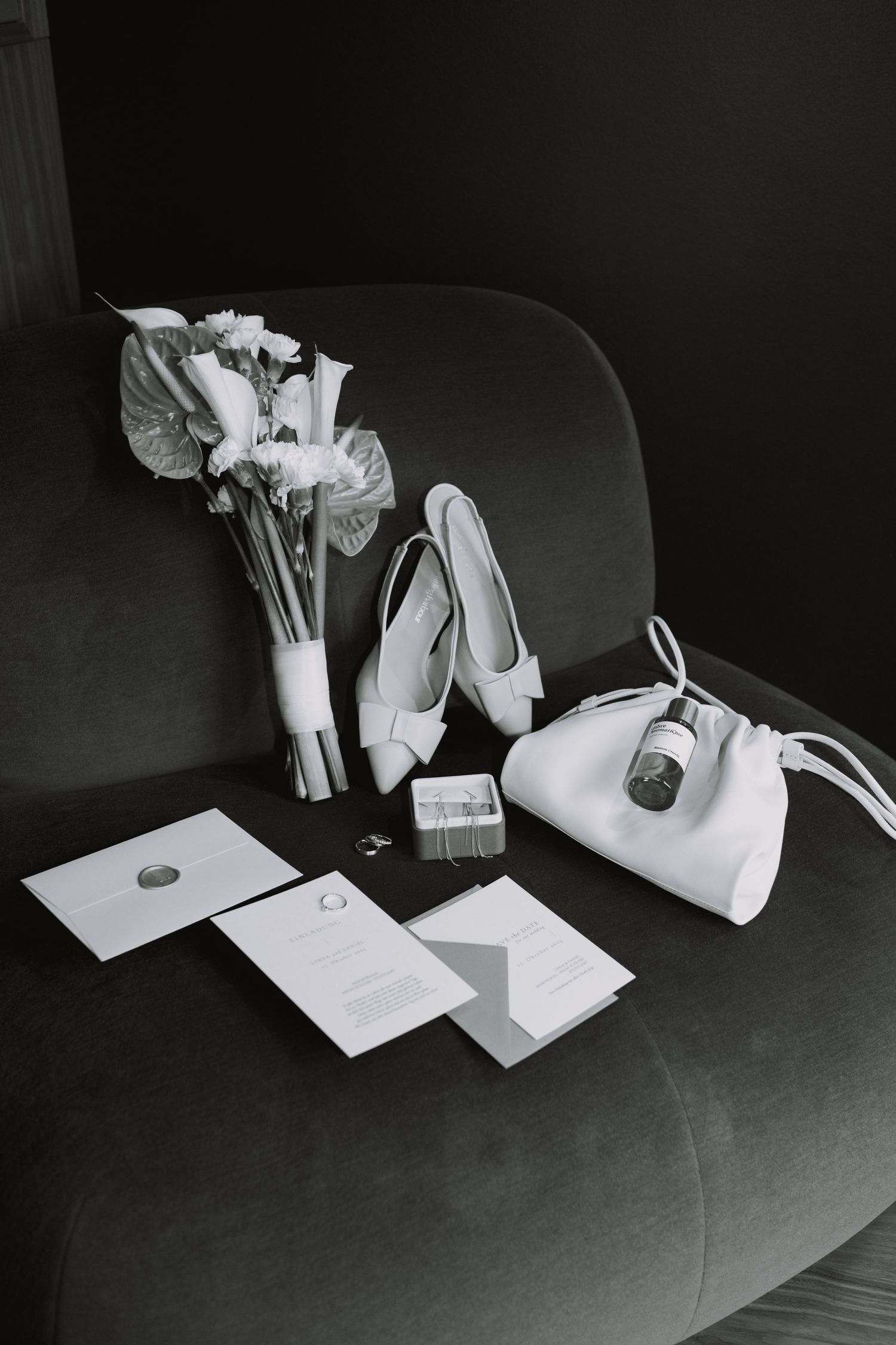 Black and white still life of wedding accessories and documents arranged on a dark surface.