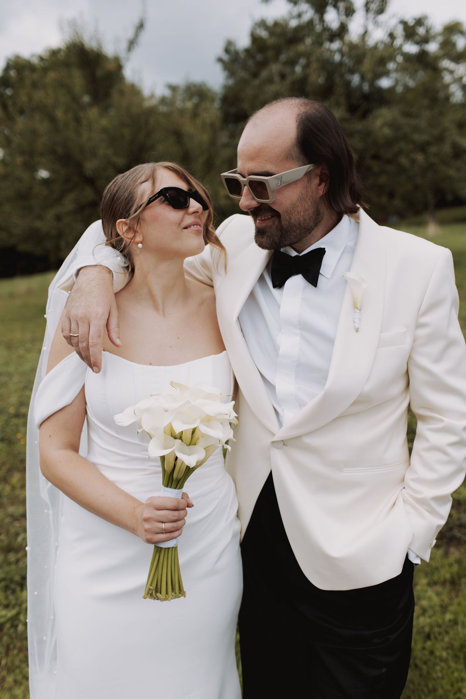 Wedding couple in white formal attire embracing while holding a bouquet of white flowers.