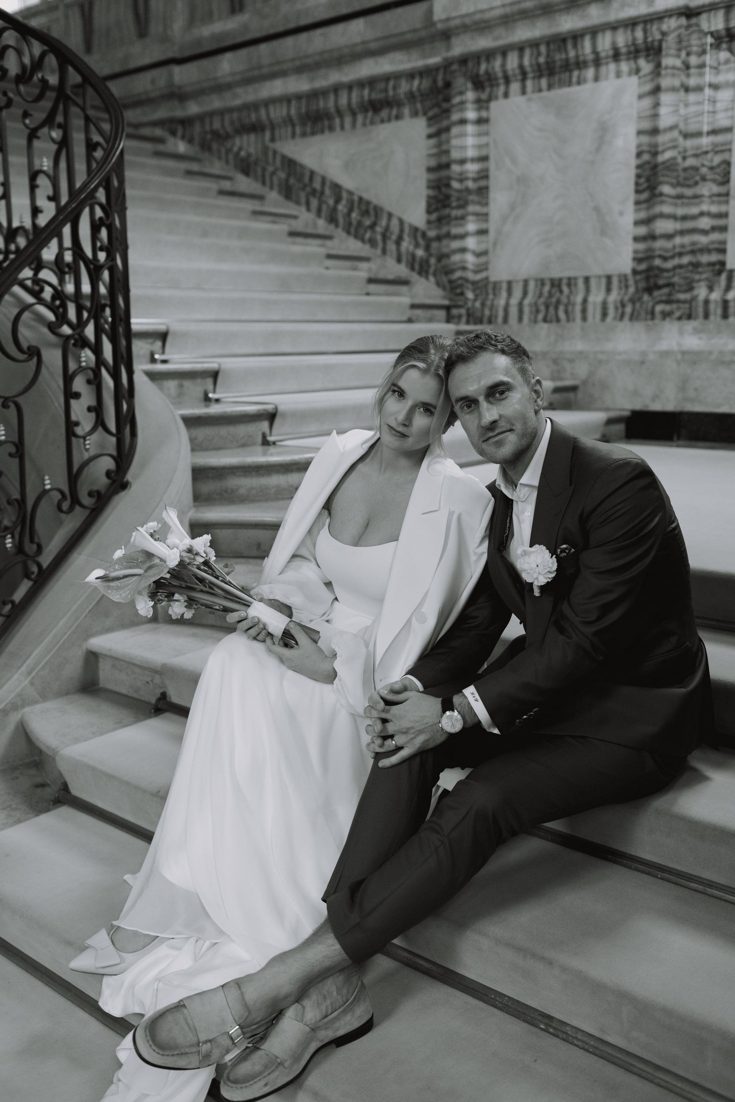 Black and white wedding photo on grand staircase with ornate iron railing.