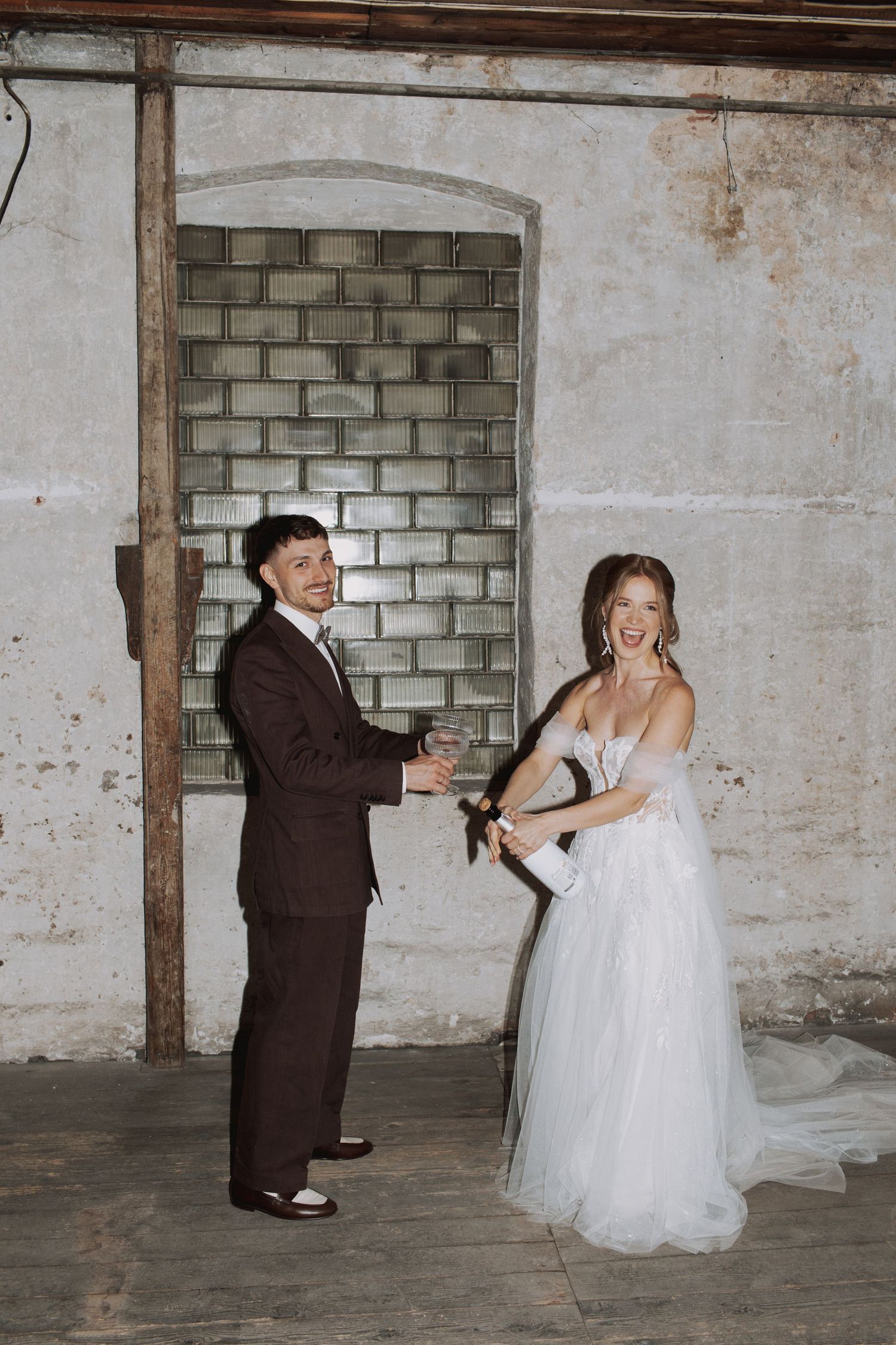 Playful wedding couple dancing and posing in an industrial space with brick walls.