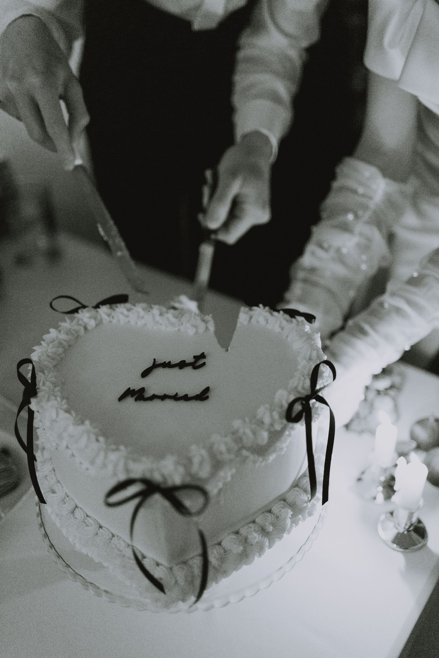 Black and white photo of cutting a white wedding cake with delicate piping.