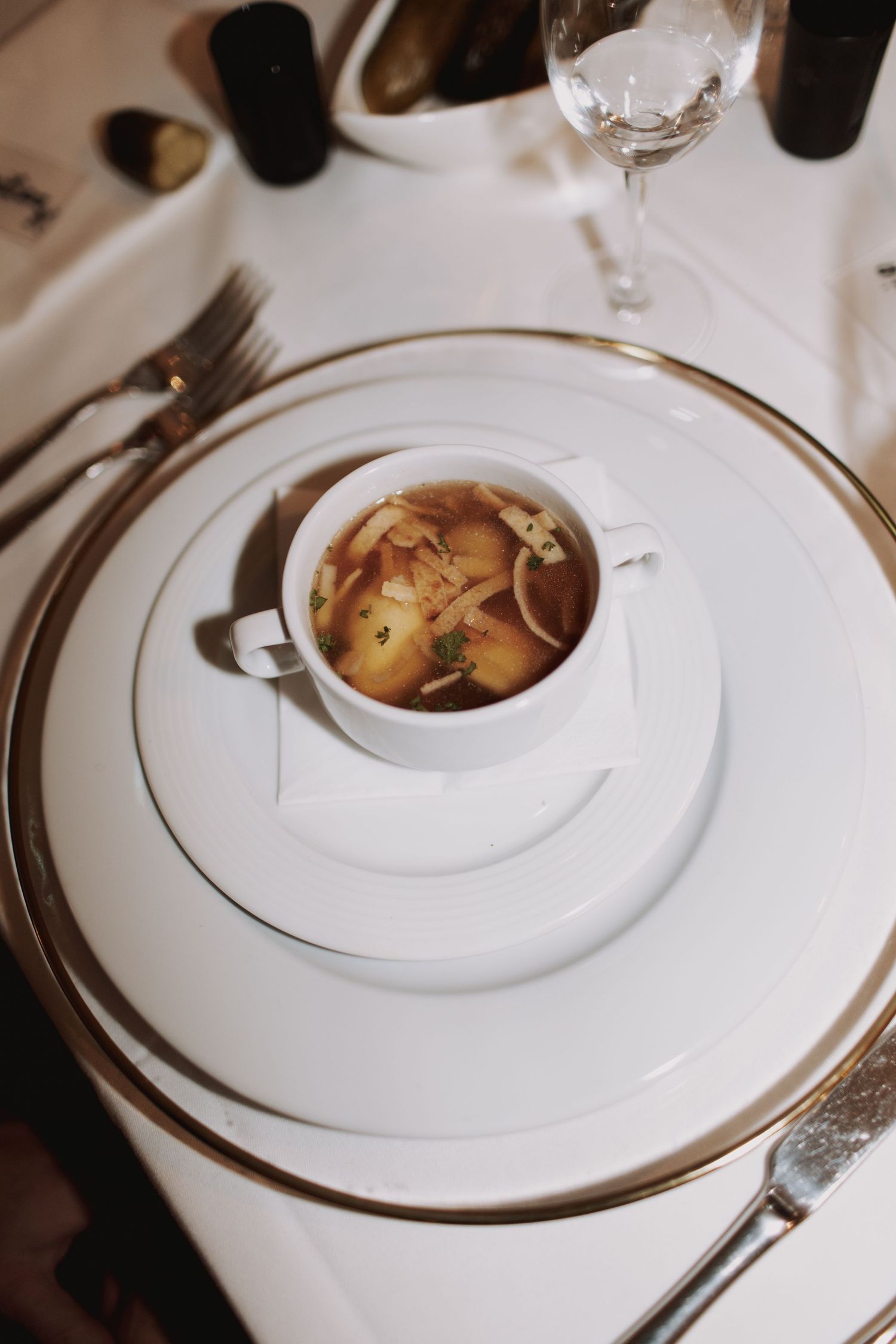 Elegant white dinner plates with gold trim and served food at a formal wedding reception.
