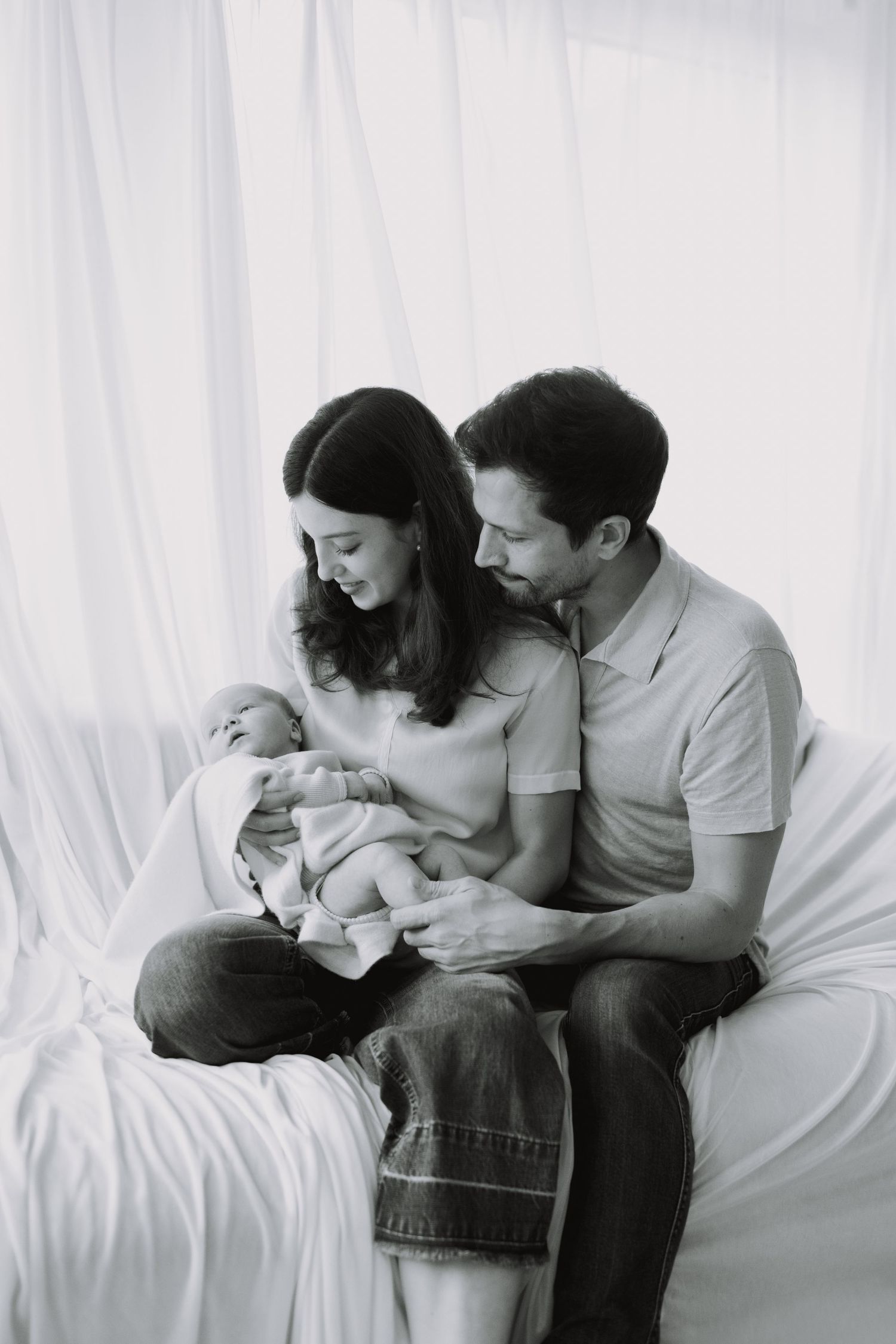 Black and white series of a family sharing intimate moments together on white bedding.