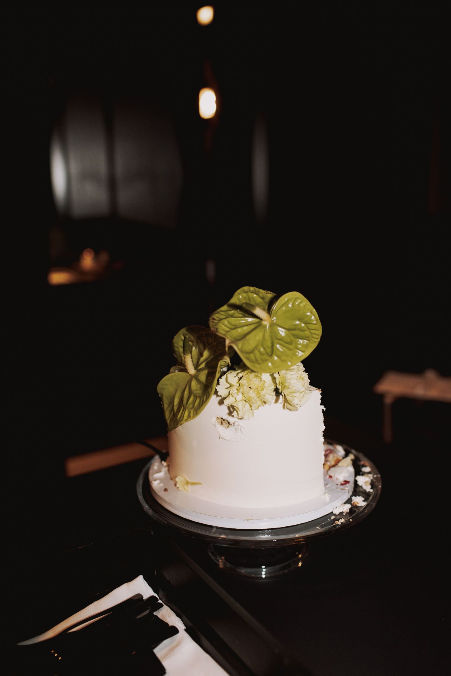 White wedding cake decorated with green leaves in dim lighting.