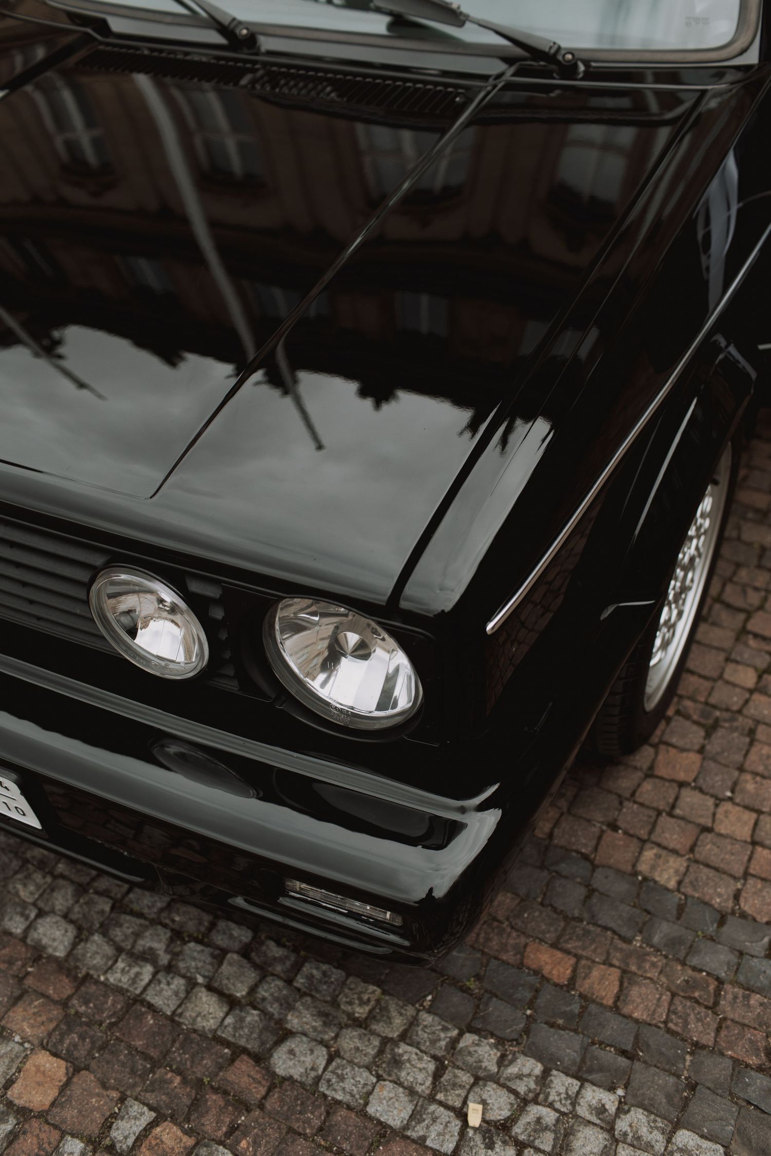 Front view of a classic black vintage car showing its distinctive headlights on cobblestone pavement.