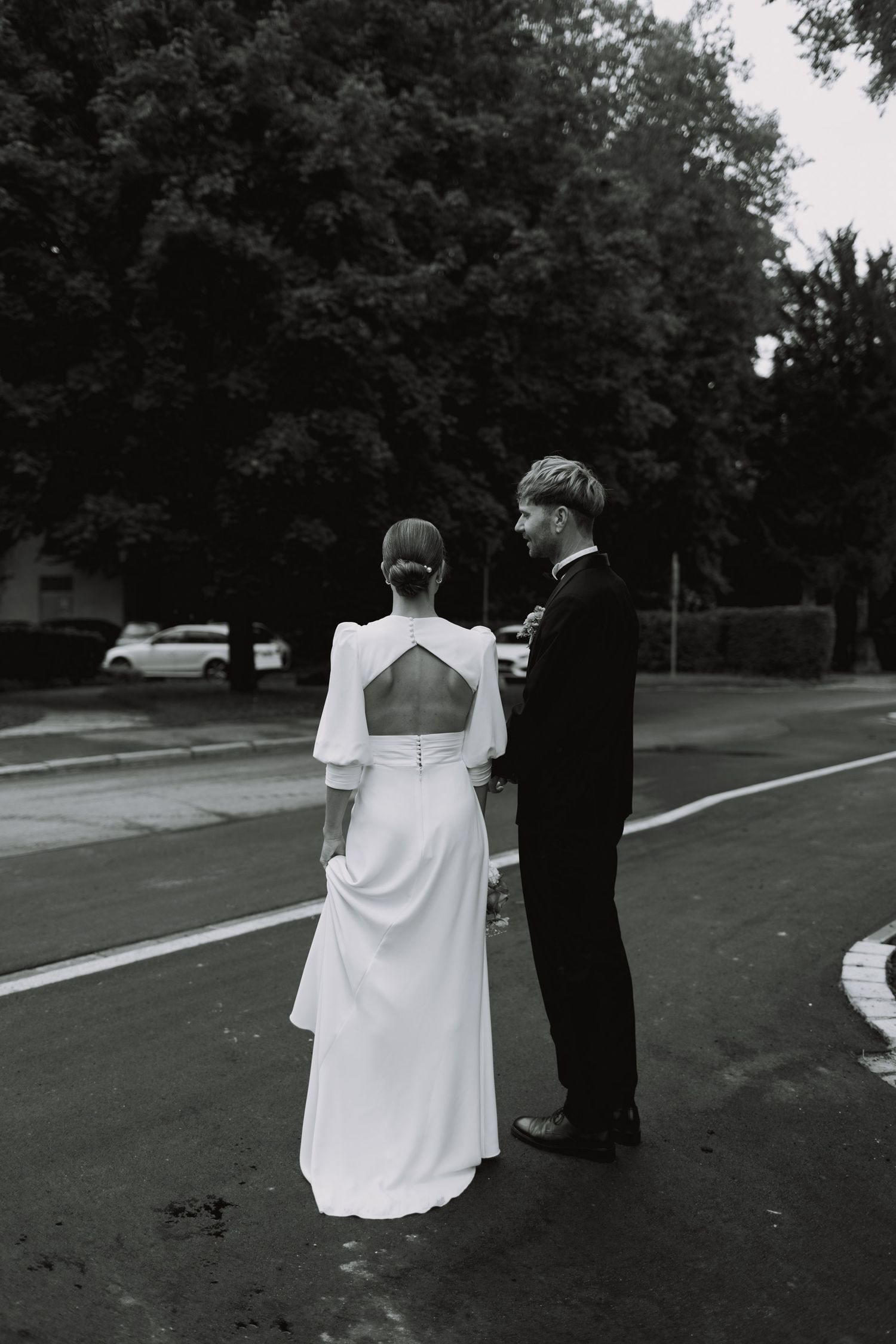 Artistic black and white photo of a couple walking outdoors in wedding attire.